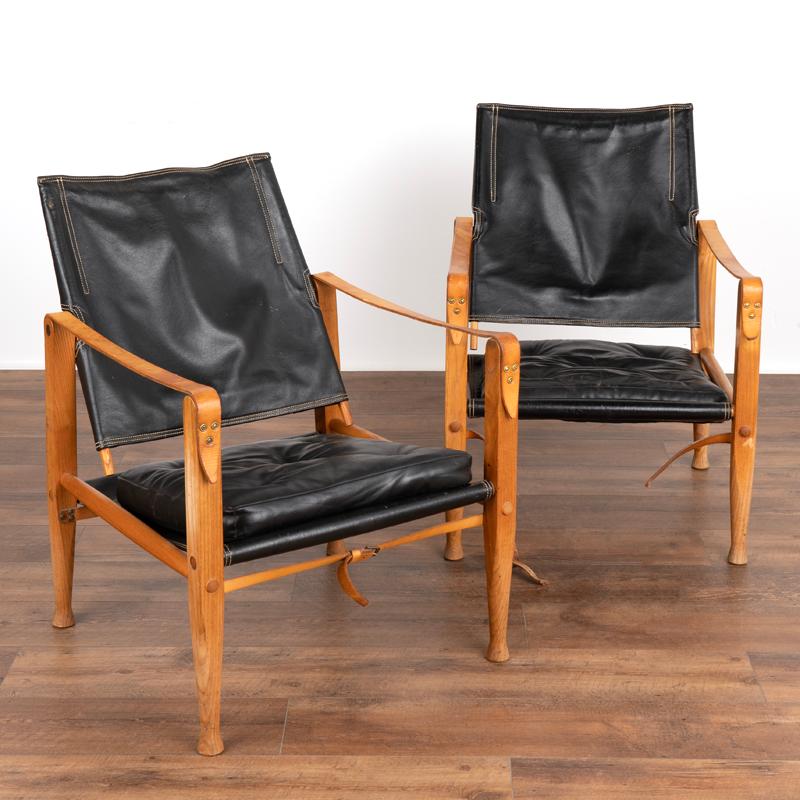 This handsome pair of original mid-century modern safari chairs were designed by Kaare Klint (1888-1954) in 1933 and manufactured at Rud Rasmussen's Carpentry. The vintage black leather is accented by original white stitching and has traditional