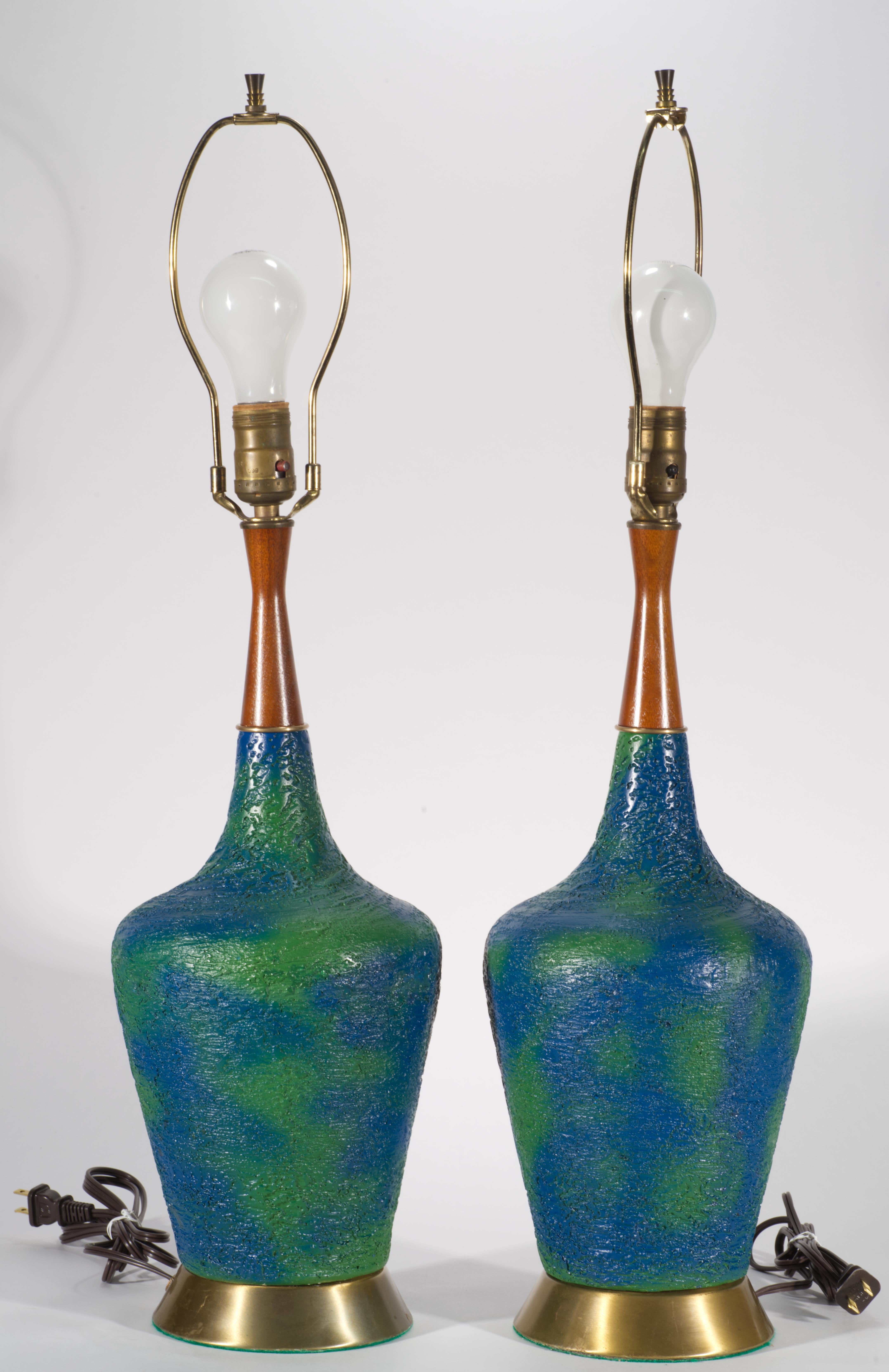 Cette paire de lampes de table vintage en céramique présente une forme moderniste épurée avec des cols allongés en bois massif sculpté, décorés de glaçures bleues et vertes, et montés sur des bases rondes en laiton. Les couleurs bleues et vertes