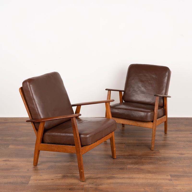 This pair of arm chairs show off the clean lines of mid-century craftsmanship and style. The smooth arms are made of teak, while the rest of the frame is in contrasting oak. In good used condition, the original brown leather shows typical signs of