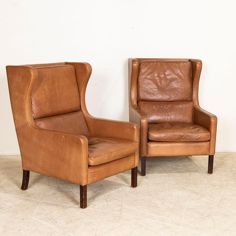 Pair of Mid-Century Modern ear flap armchairs upholstered in light brown vintage leather by Mogens Hansen. Each of these comfortable chairs has 3 loose cushions and solid beech wood legs. General age-related signs of wear include impressions,