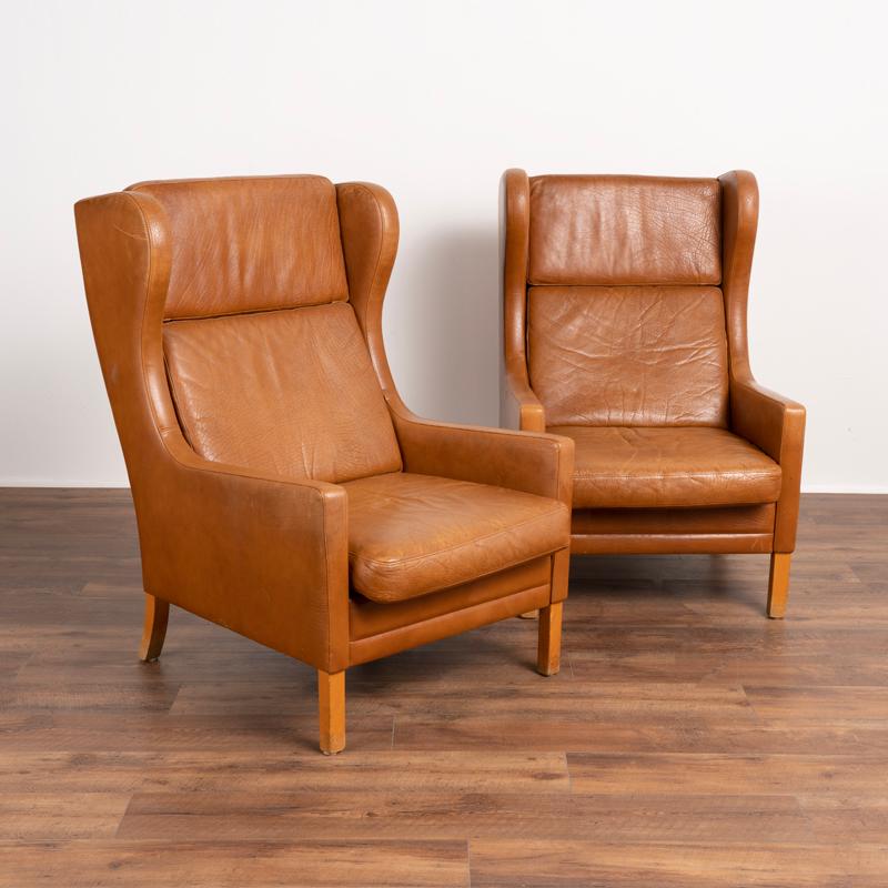 Pair of mid century modern ear flap armchairs upholstered in light brown or cognac vintage leather by Mogens Hansen. Each of these comfortable chairs has 2 loose cushions (headrest and back cushion are attached to each other and remove) and solid