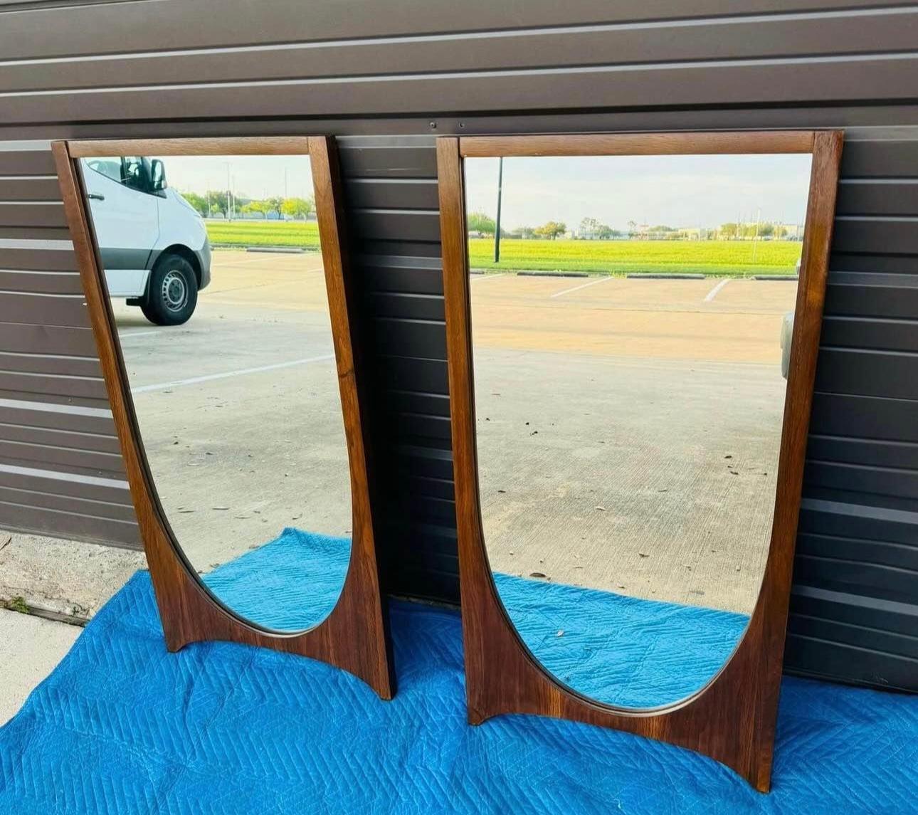Beautiful pair of refinished Broyhill Brasilia mirrors, a well-known mid-century modern design inspired by the architecture of Brasília, Brazil.

Key Features:
	•	Shape & Frame: The mirrors have a striking walnut wood frame with a unique sculptural