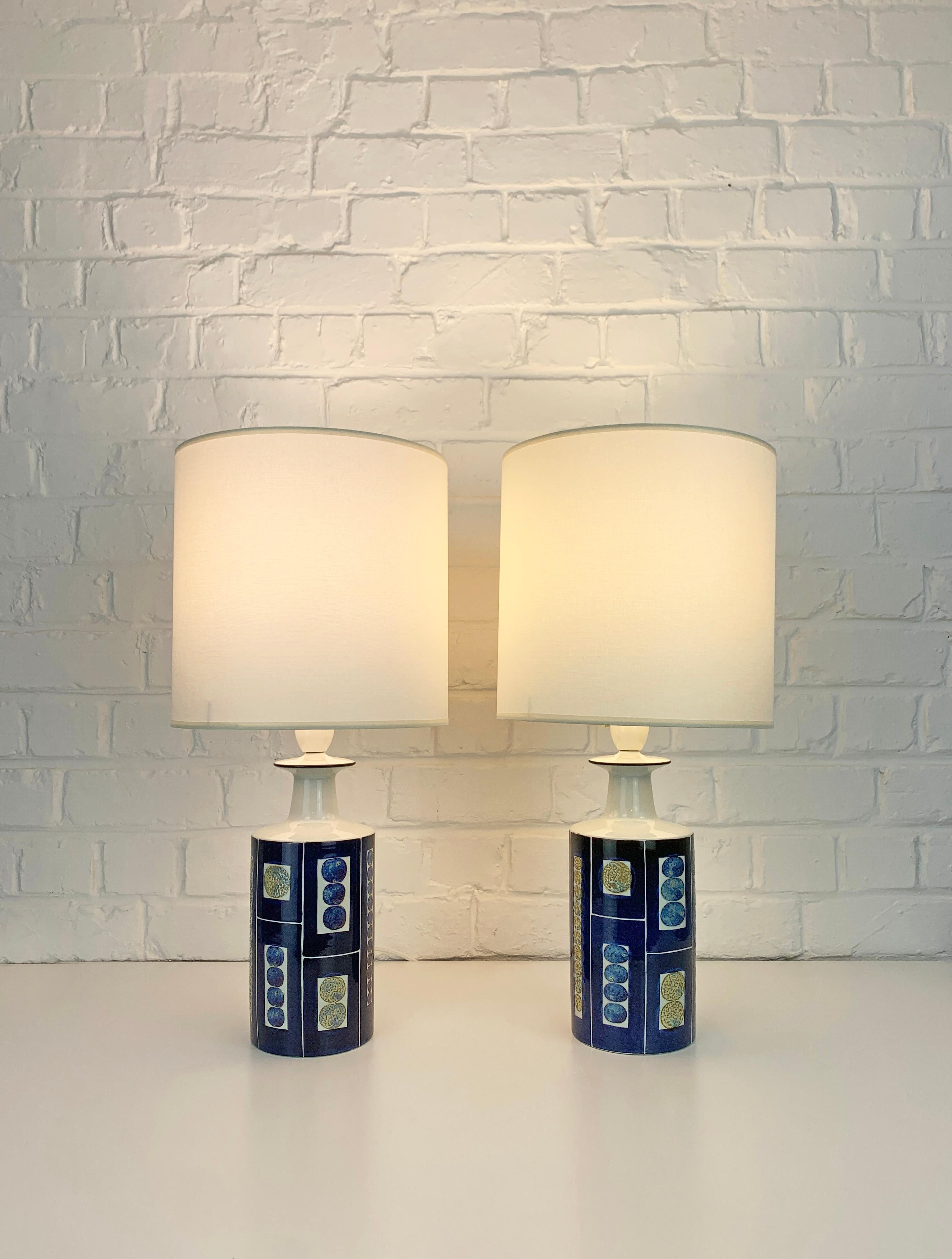 Pair danish hand-painted table lamps from the late 1960s or early 1970s. 

Impressive bold graphic design by Inge-Lise Koefoed, featuring a decor in dark blue with greyish / beige elements. 

Manufactured by Royal Copenhagen and sold by Fog & Mørup,