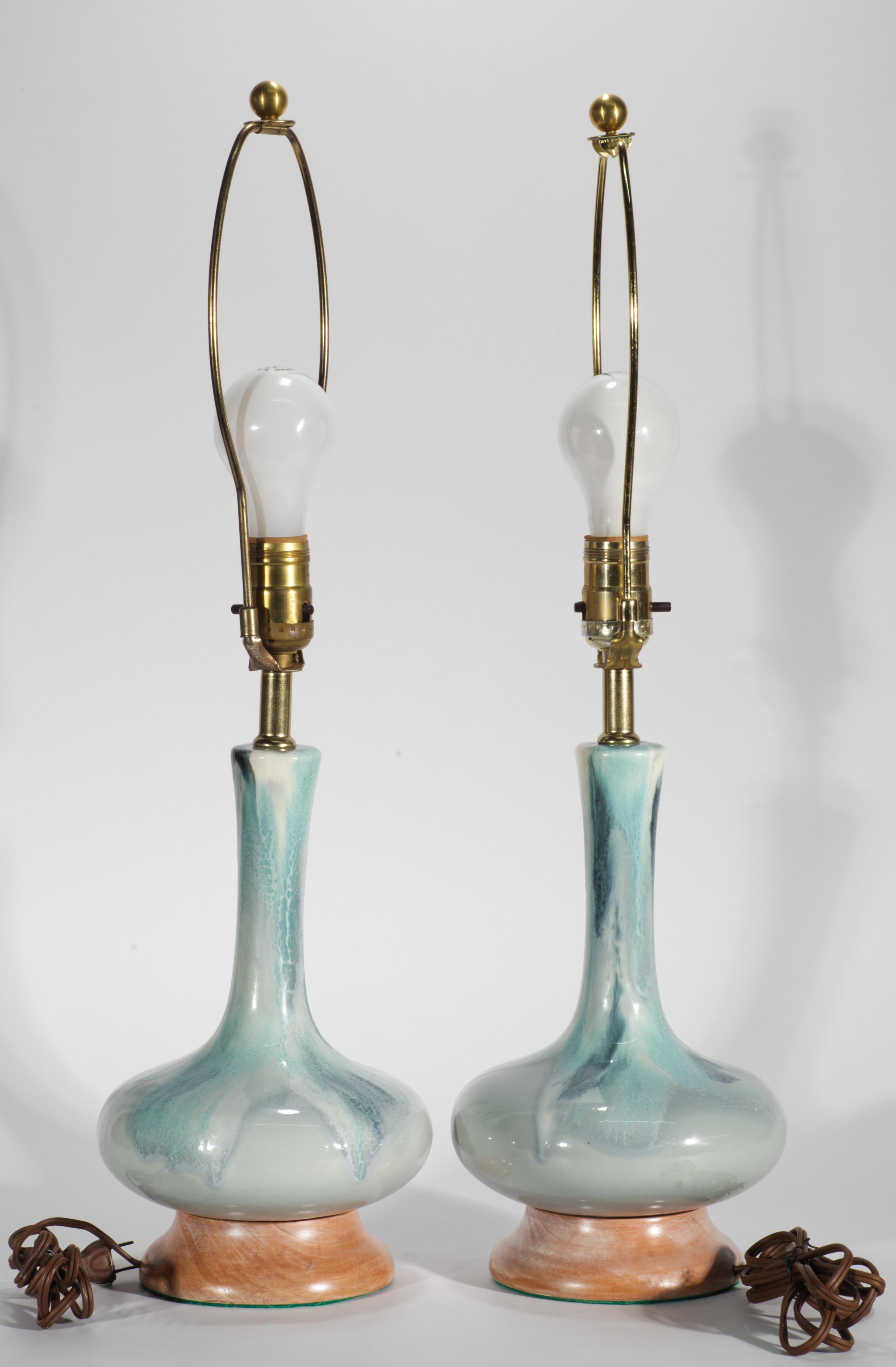  Cette paire de lampes de table vintage en céramique présente une forme bulbeuse moderniste avec un col allongé, décorée d'une glaçure flammée bleue et montée sur des bases en bois massif. D'élégants éléments de glaçure goutte à goutte ton sur ton