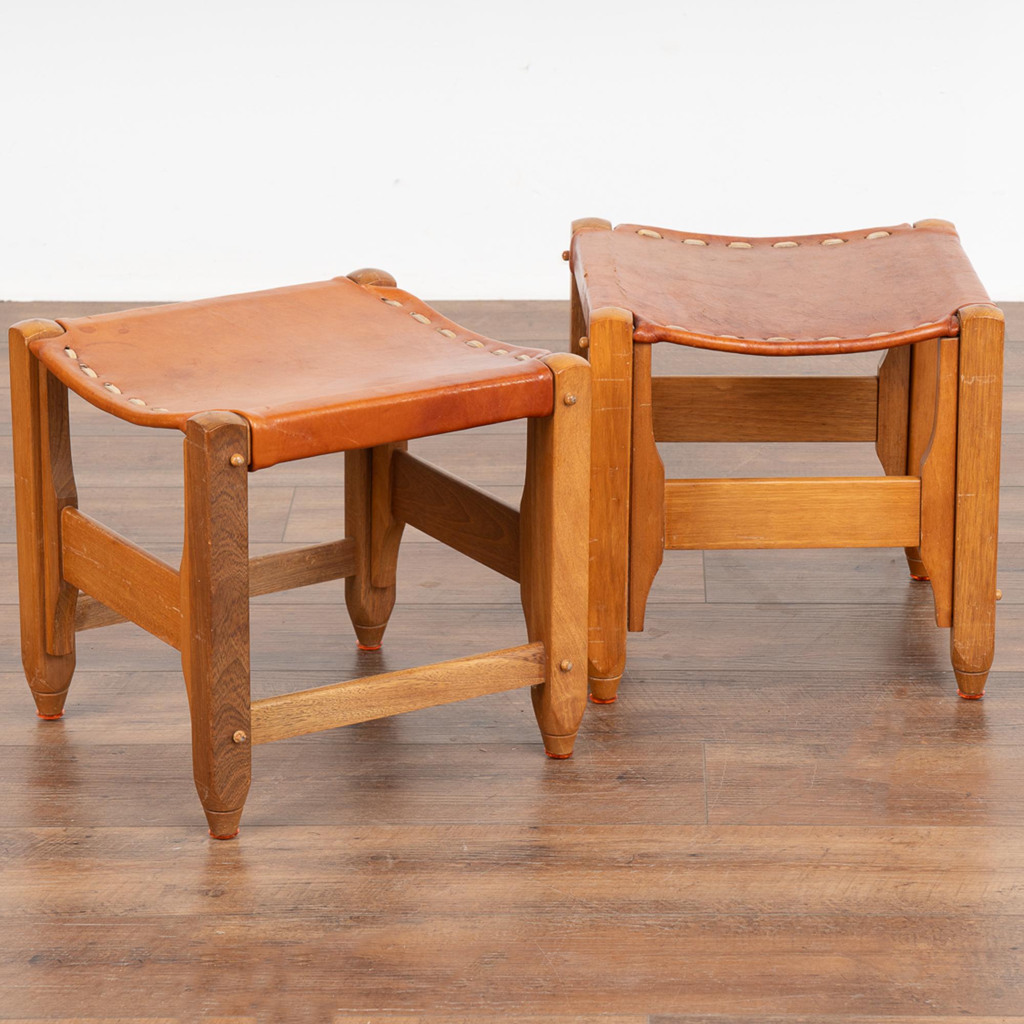 Pair, mid-century modern leather stools with hardwood frame. Note the contrasting leather stitching that adds to the retro look of the leather seats.
Vintage brown leather seats show crackles, stains, scratches, etc. and will likely benefit from