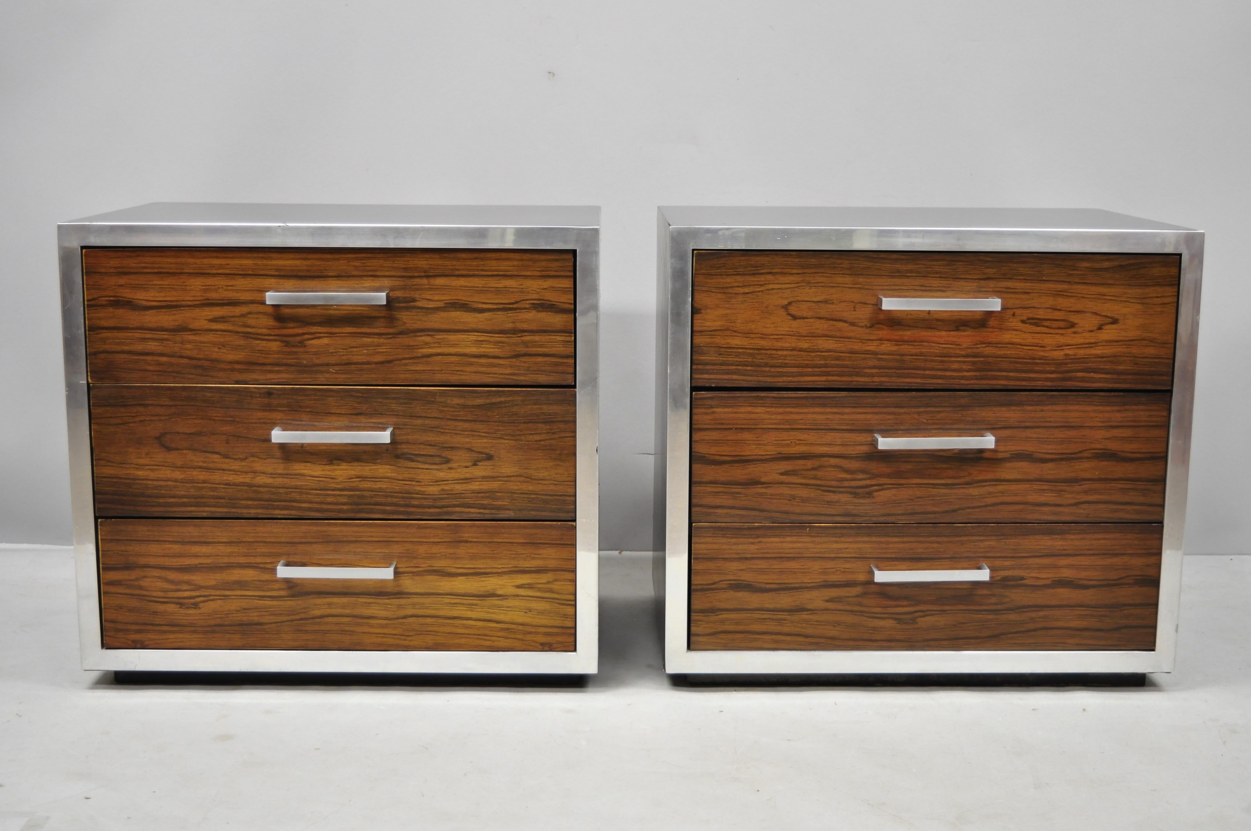 Pair of Mid-Century Modern rosewood and chrome 3-drawer nightstands after Milo Baughman. Items feature chrome trim and handles, black laminate top and sides, rosewood veneer drawer fronts, 3 dovetailed drawers, clean modernist lines, great style and