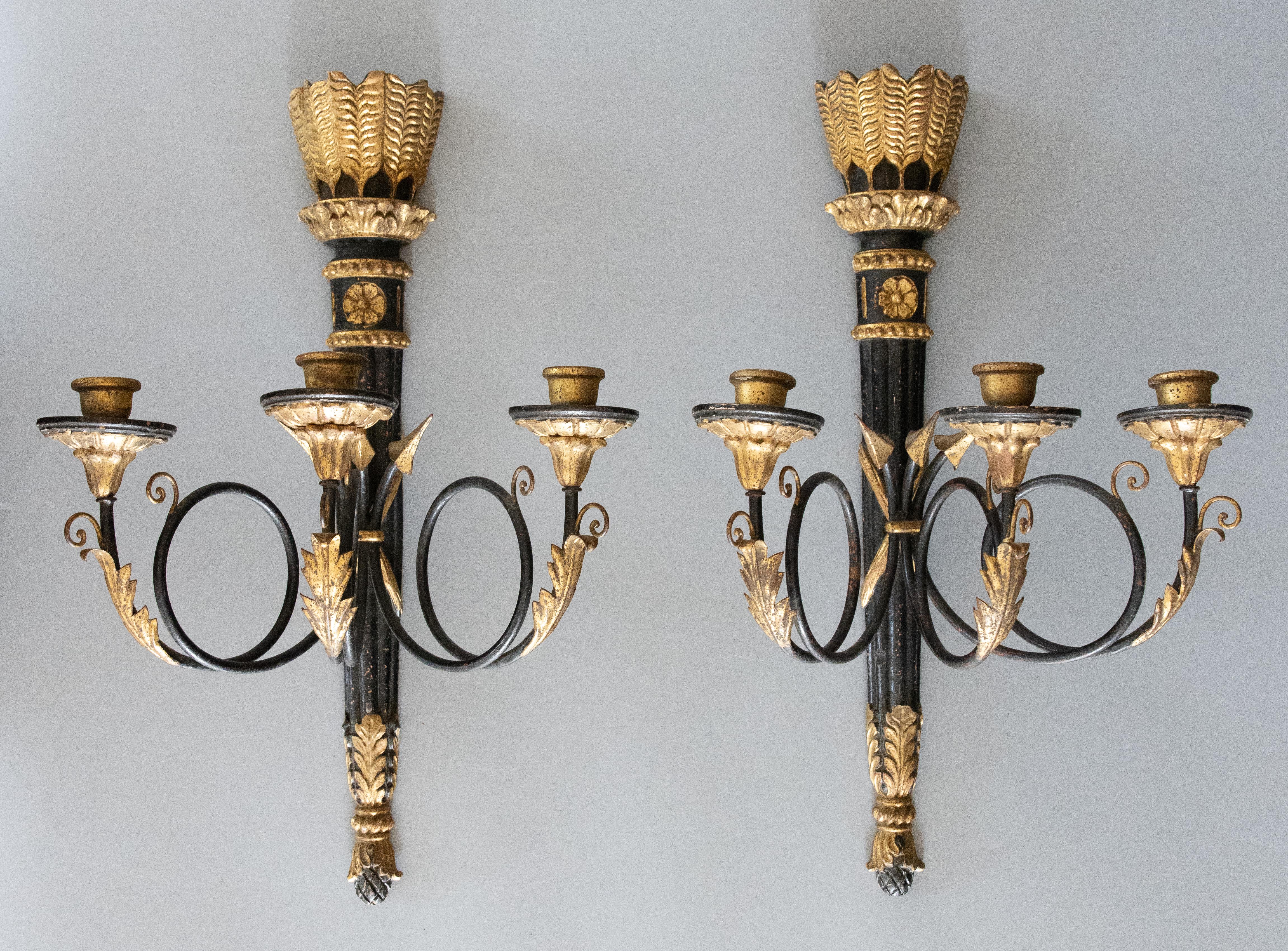 A gorgeous pair of Italian Neoclassical style ebonized and gilded wood and tole three-arm candle sconces, circa 1950. 