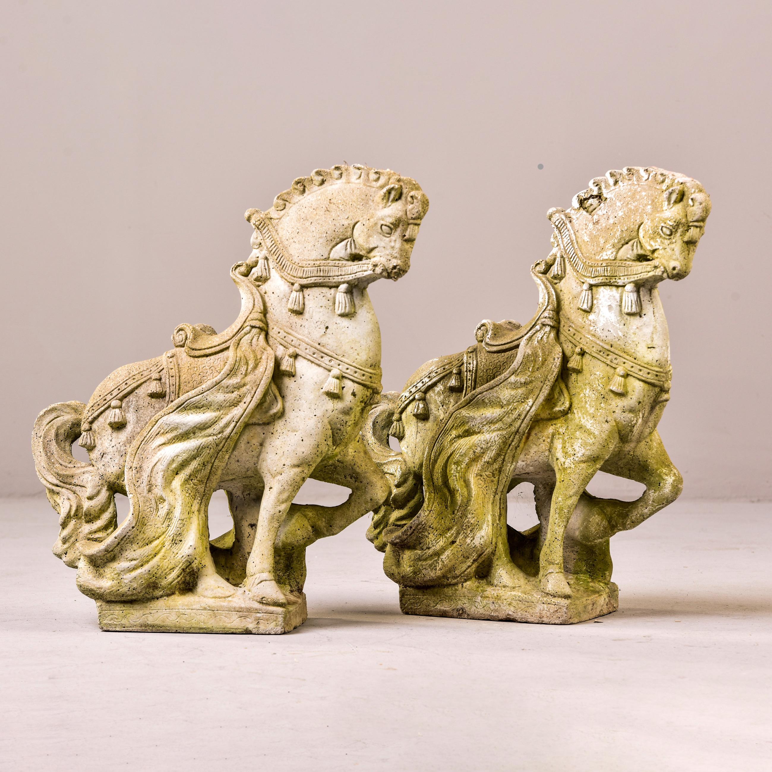 Circa 1950s pair of cast cement garden statues in the form of Spanish horses with tasseled manes. Statues have scattered surface wear and patina/moss. Unknown maker. Sold and priced as a pair.