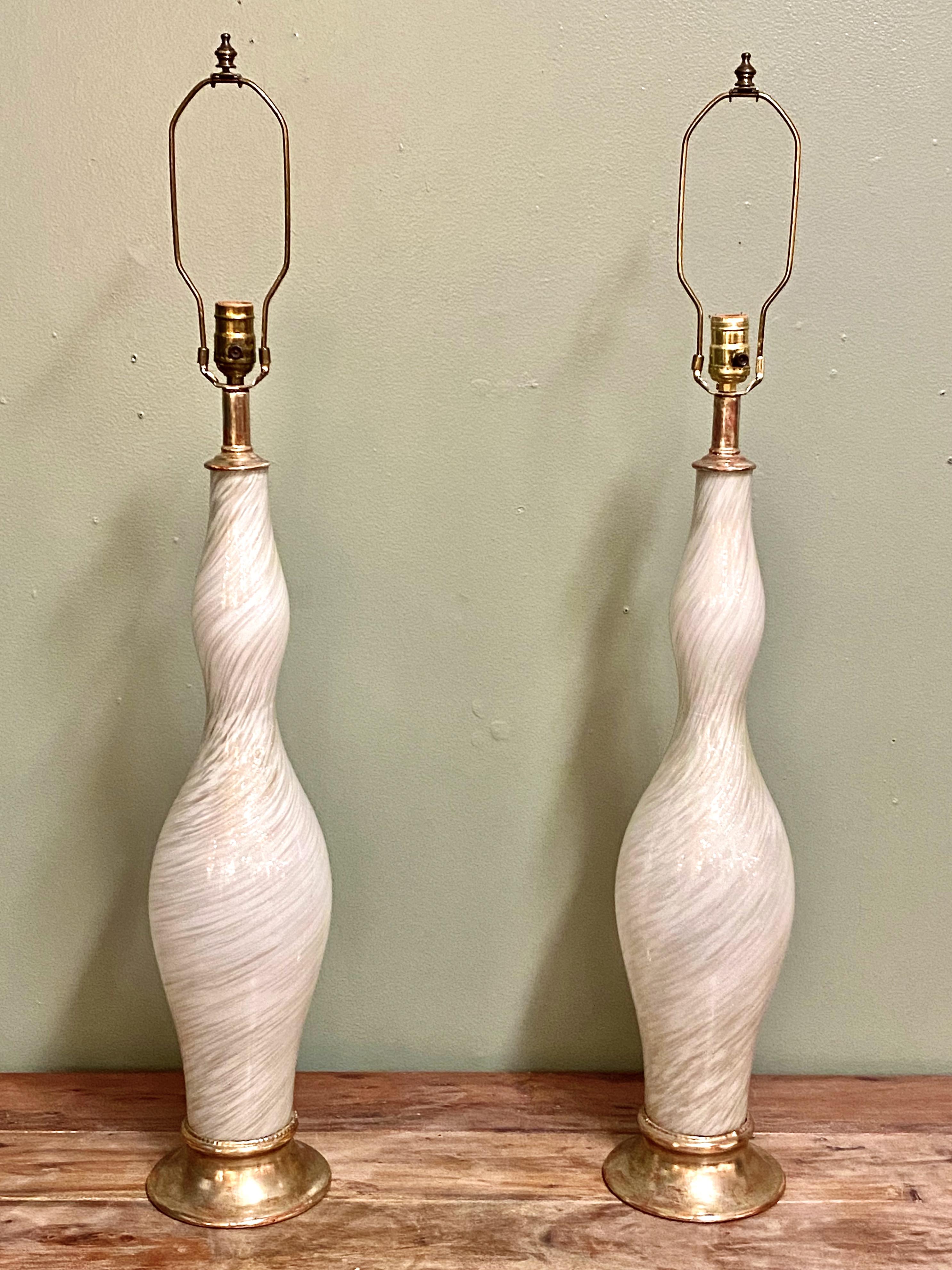 This is a stunning pair of mid-century Murano lamps that have been accented with gold leaf bases. The white swirled and gold powder-infused glass is in excellent condition and unusual in its height, measuring 29 inches to the base of the socket. The