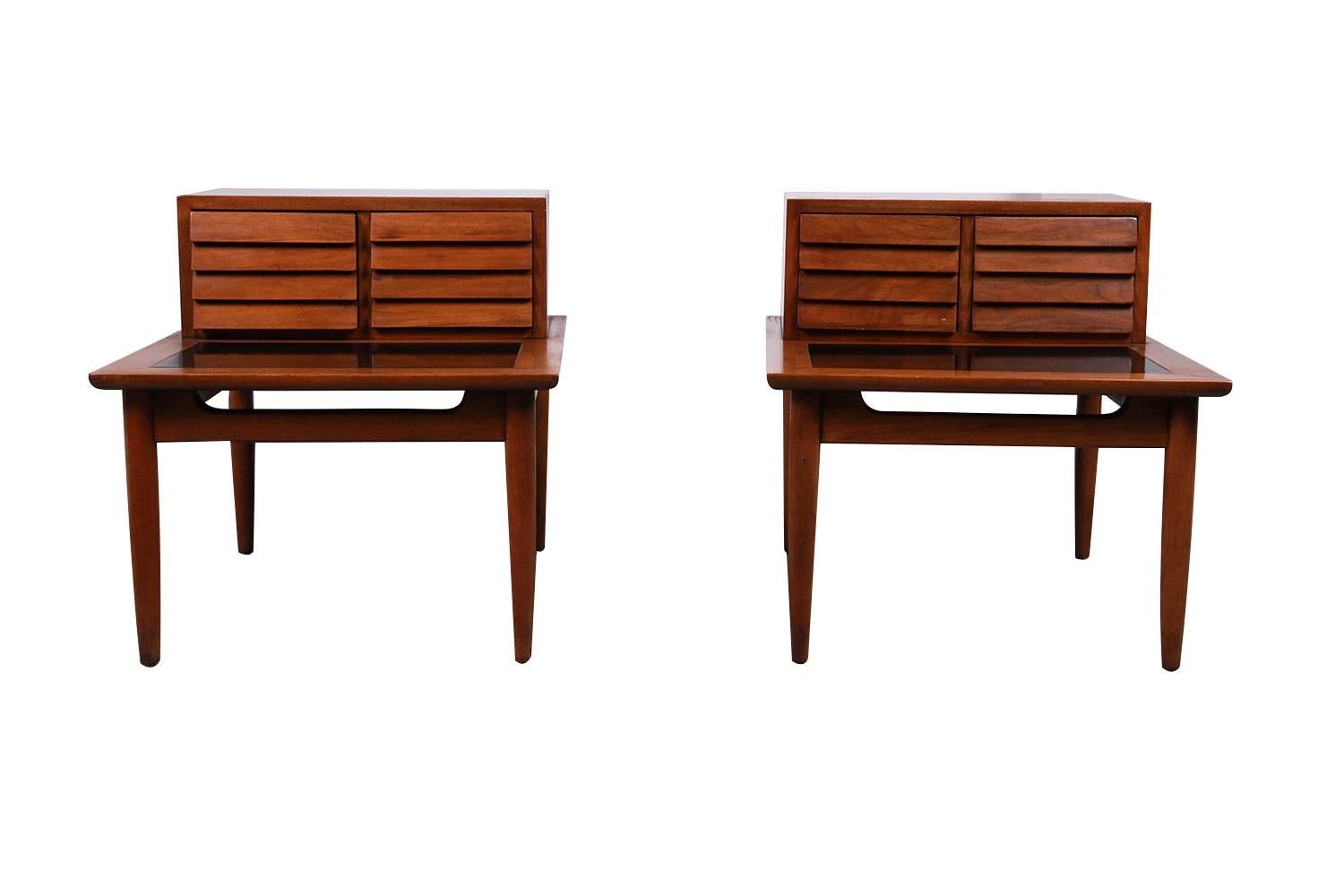 Striking pair of architectural Mid-Century Modern two-tier walnut nightstands or end tables by American of Martinsville, circa 1960's. “Dania” line, designed by Merton Gershun, is one of the most esteemed furniture producers of the Mid-century era.