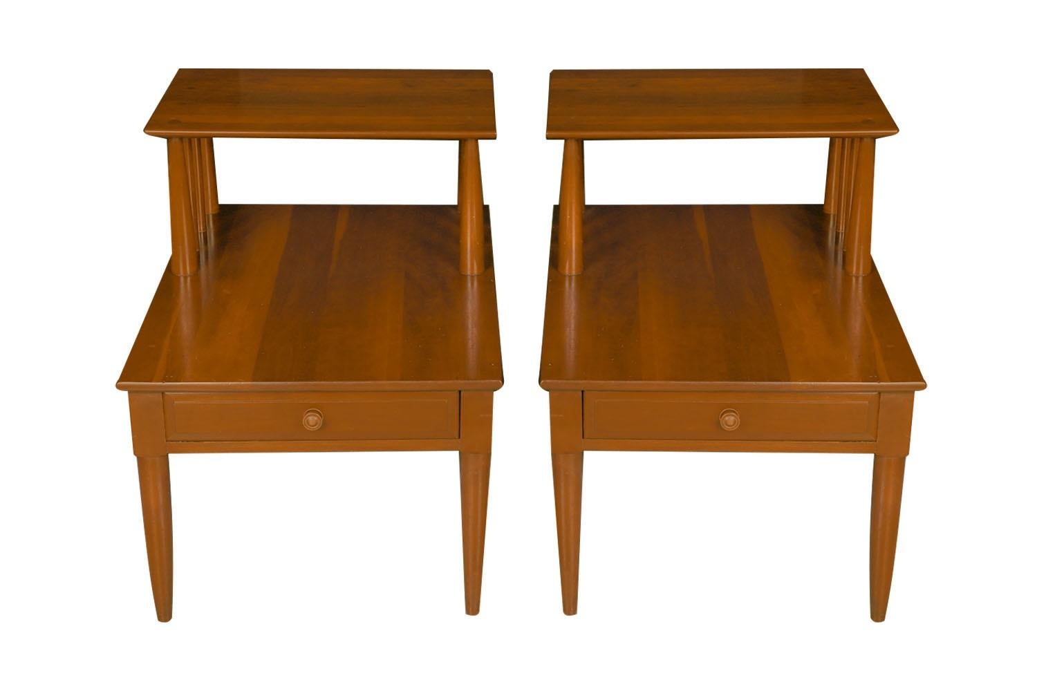 Striking pair of architectural Mid-Century Modern two-tier solid cherry nightstands or end tables by Willett furniture, circa 1960’s. Multipurpose tables each feature a two tier minimalist design with one deep dovetailed drawer. Maker’s name stamped