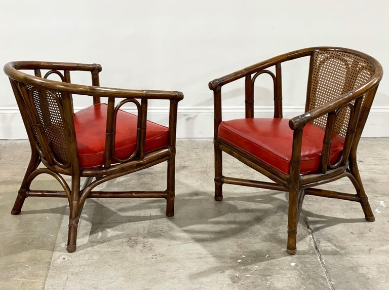 Exquisite pair of vintage McGuire organic modern barrel back arm chairs by John and Elinor McGuire. Featuring original ox blood tone naugahyde seats - a rare original colorway. Each chair retains their brass McGuire badges as well as their original
