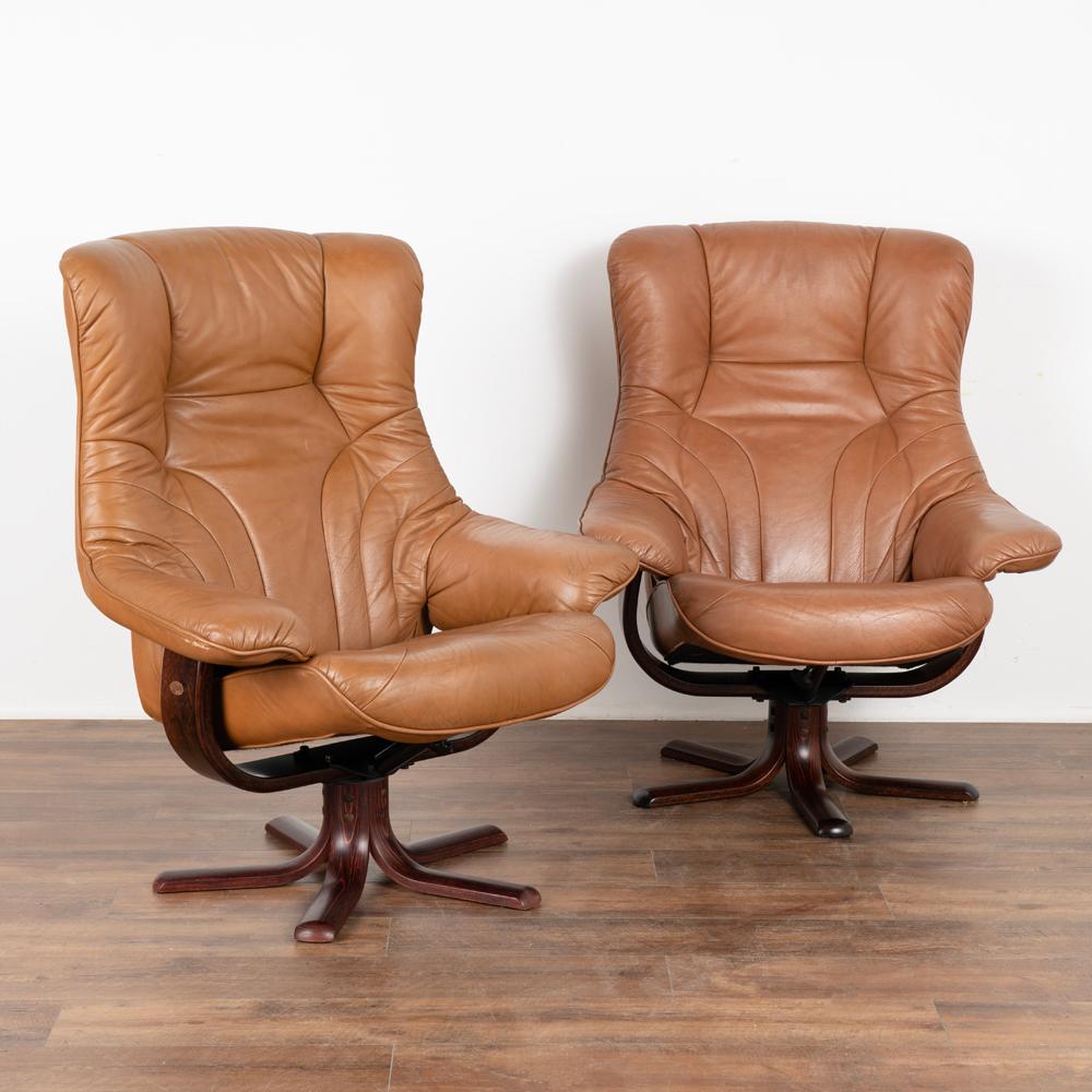 Pair, Mid-Century Modern reclining arm chairs on swivel base made of beech by Stouby of Denmark.
Upholstered patinated brown leather. Sold in vintage used condition; this pair sits very comfortably.
Age related use seen in the leather including
