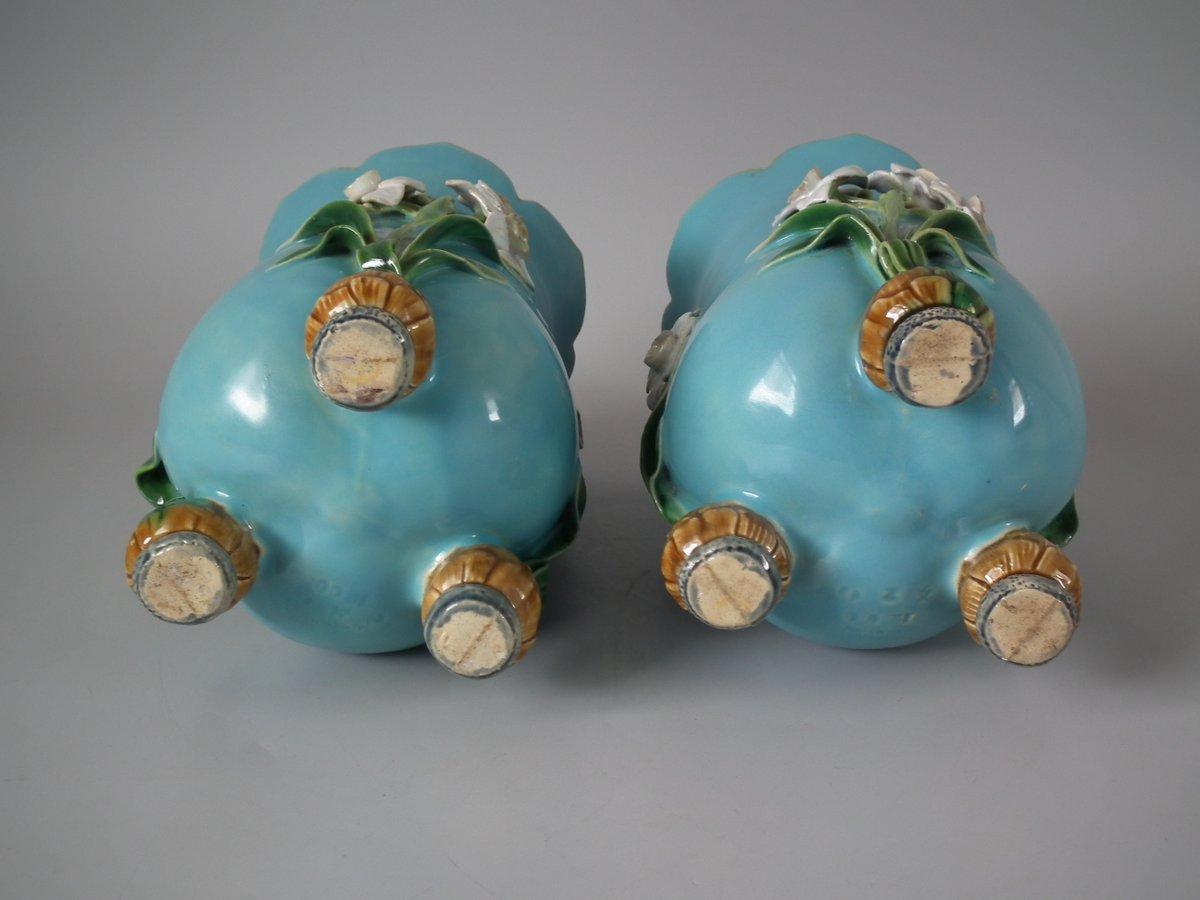 Pair of Minton Majolica vases which feature daffodils stood on bulb feet. Turquoise ground version. Colouration: turquoise, green, white, are predominant. The piece bears maker's marks for the Minton pottery. Bears a pattern number, '1200'. Marks
