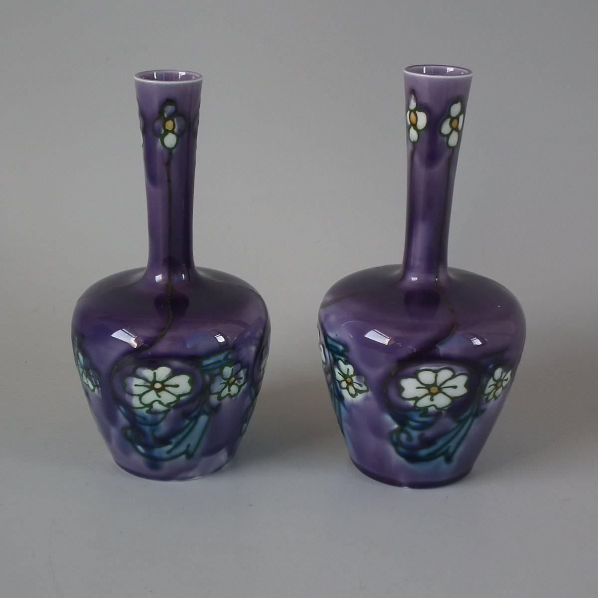 Pair of Minton Secessionist fluted vases, decorated with typical Art Nouveau stylized flowers and leaves. Green tube lining detail, on purple ground. Printed maker's marks 'MINTONS LTD No.33' to the underside.