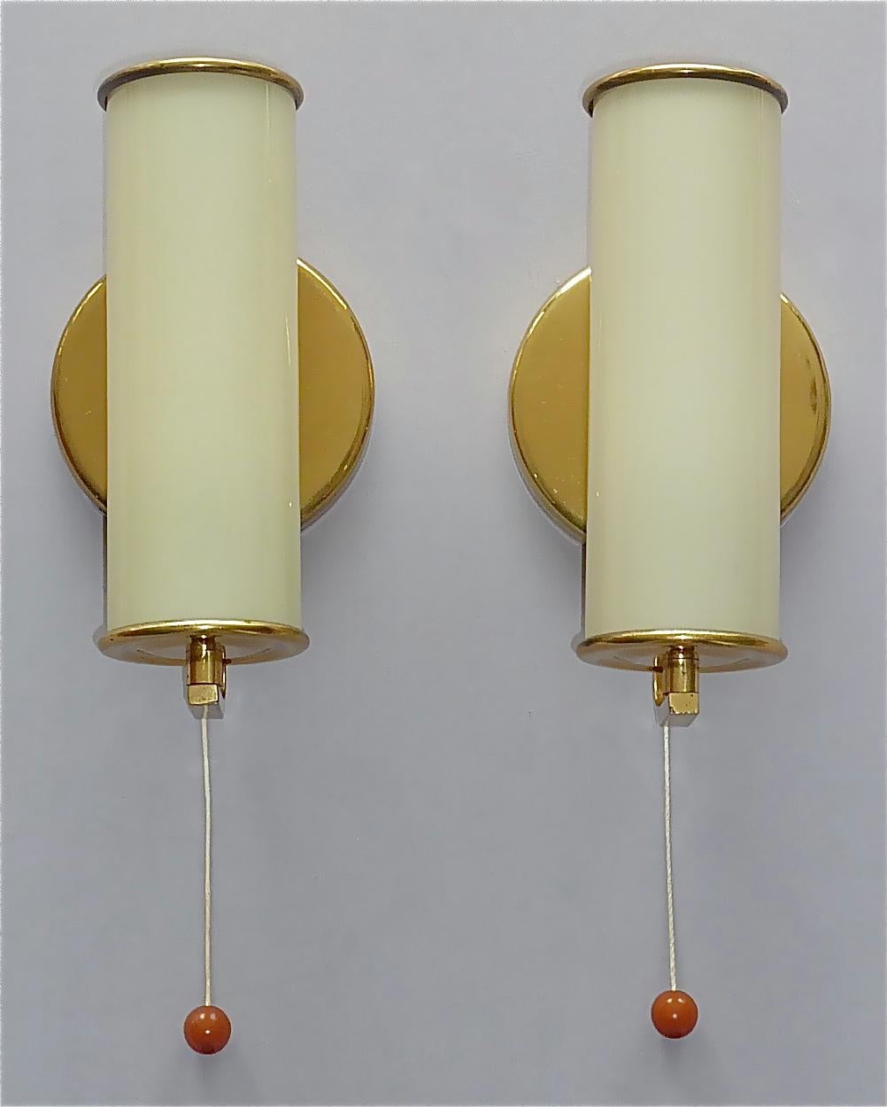 Beautiful german Bauhaus or Scandinavian modernist sconces in Paavo Tynell Taito Oy / Kalmar Style, circa 1930s to 1940s. The wall lights which are made of patinated brass with faint yellow opaline glass tubes and threat-switches with nice amber