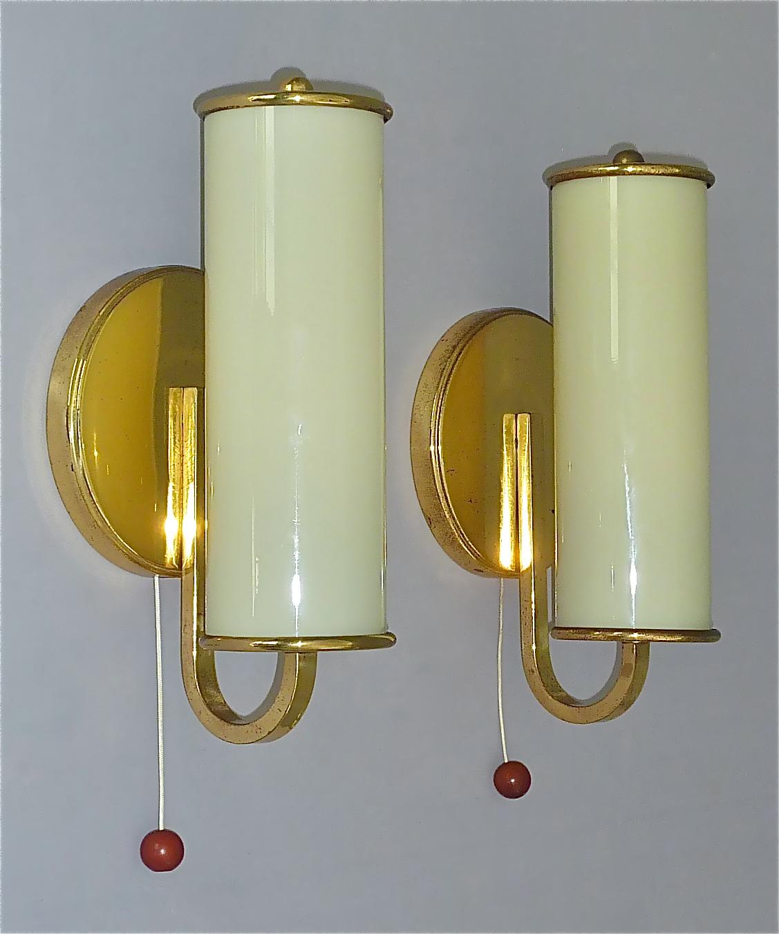 Beautiful german Bauhaus or Scandinavian modernist sconces in Paavo Tynell Taito Oy / Kalmar Style, circa 1930s to 1940s. The wall lights which are made of patinated brass with faint yellow opaline glass tubes and threat-switches with nice amber