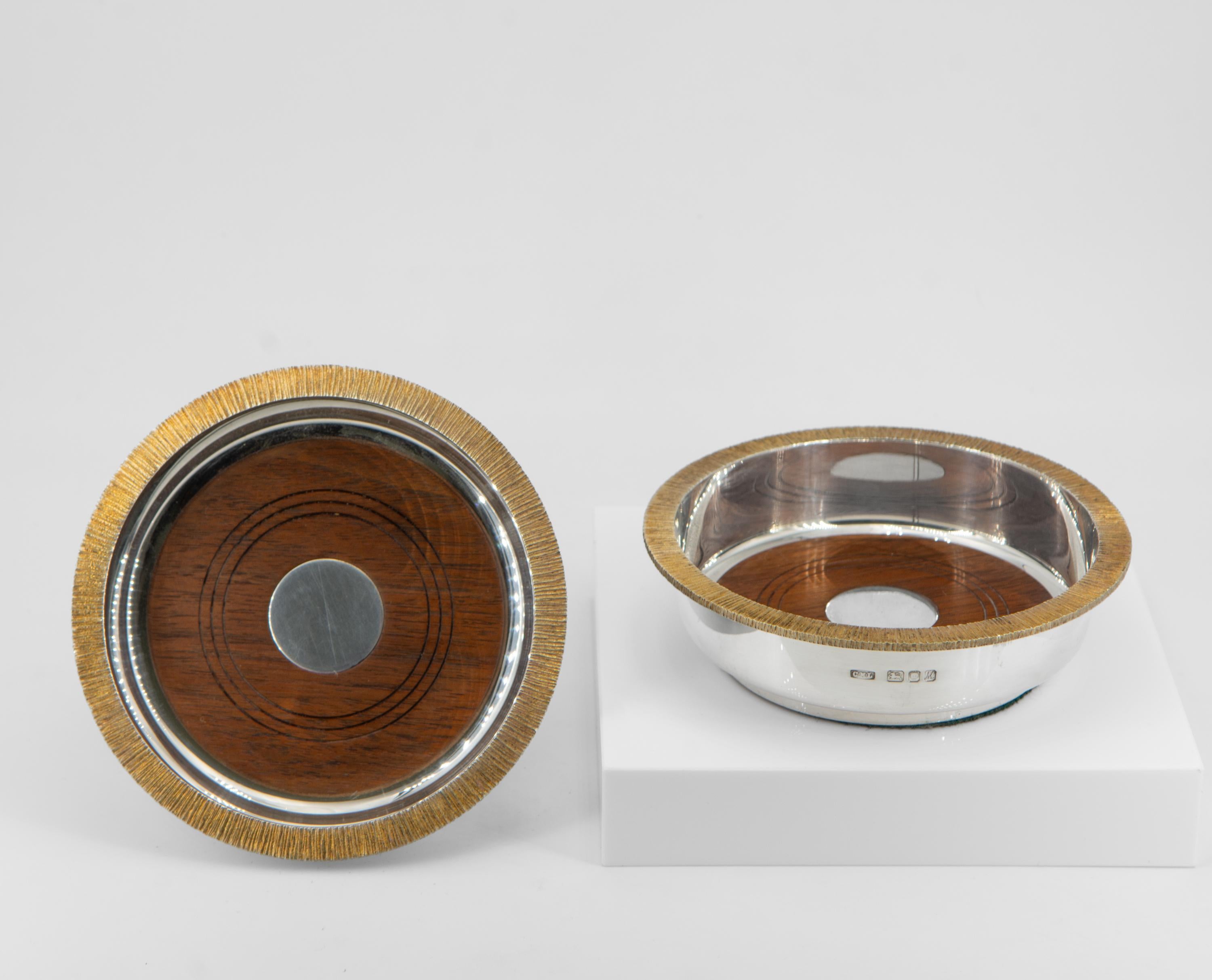 Pair Elizabeth II Modernist sterling silver & silver gilt limited edition wine coasters, London 1986 by Christopher Nigel Lawrence.  

The coasters are of circular form with contrasting naturalistic silver gilt 'bark' textured edge and inset turned