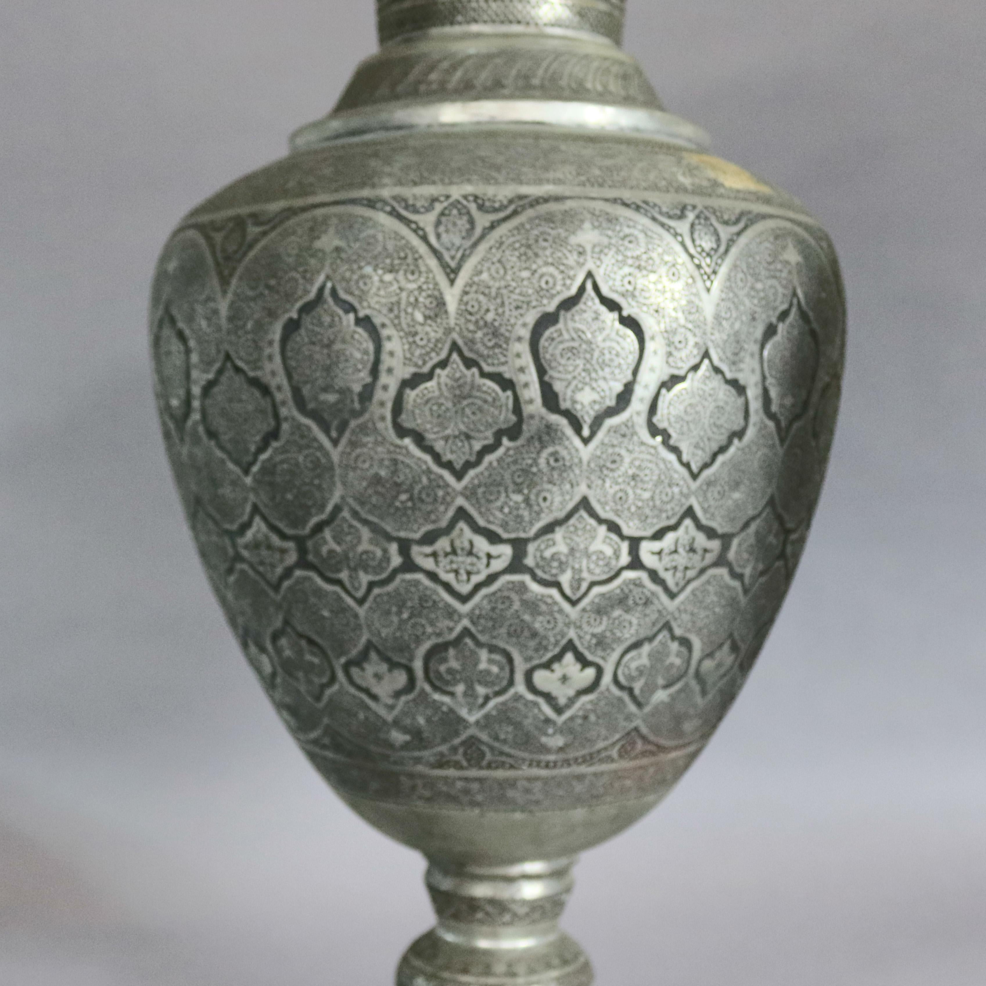 A pair of monumental Persian floor urns offer hand-hammered repeating Islamic patterns including paisley and arched geometric and arabesque designs, bulbous vessel is raised on stepped base and has neck terminating in flared mouth, 19th