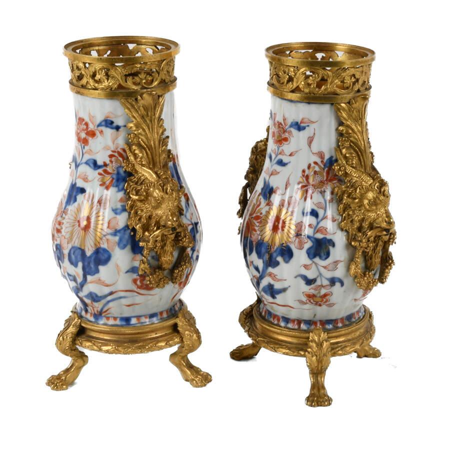 This Pair of Mounted Chinese Export Imari Vases is a stunning duo of decorative vessels that elegantly blend Eastern ceramic artistry with opulent Western-style mounts. Each vase features classic Imari floral motifs in vibrant cobalt blue, iron red,