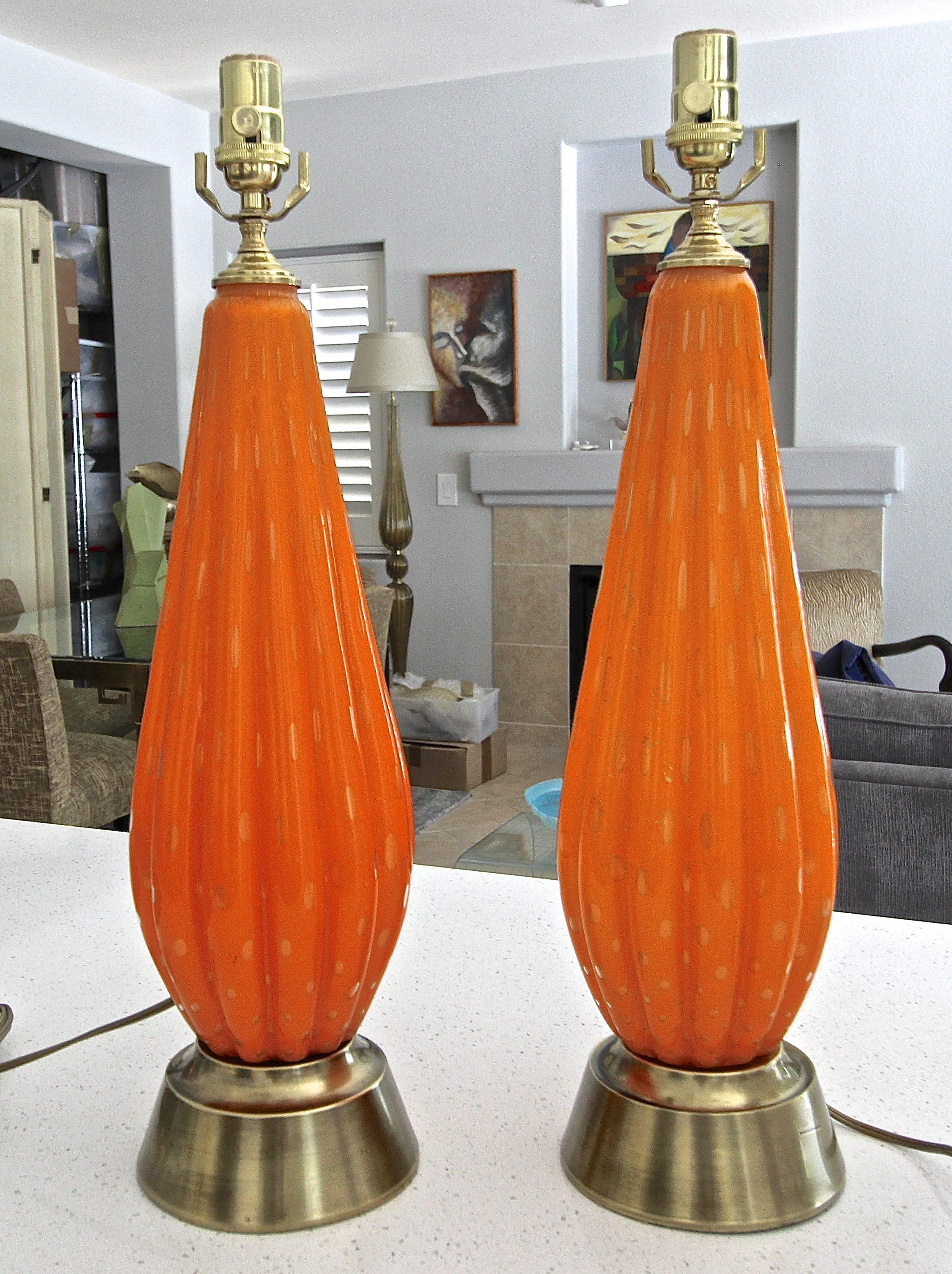 Pair of Italian Murano hand blown ribbed orange color glass table lamp with gold inclusions and controlled bubbles. The glass lamps are mounted on their original brass plated bases. Rewired with new brass 3 way socket and cord.
Measures: Glass