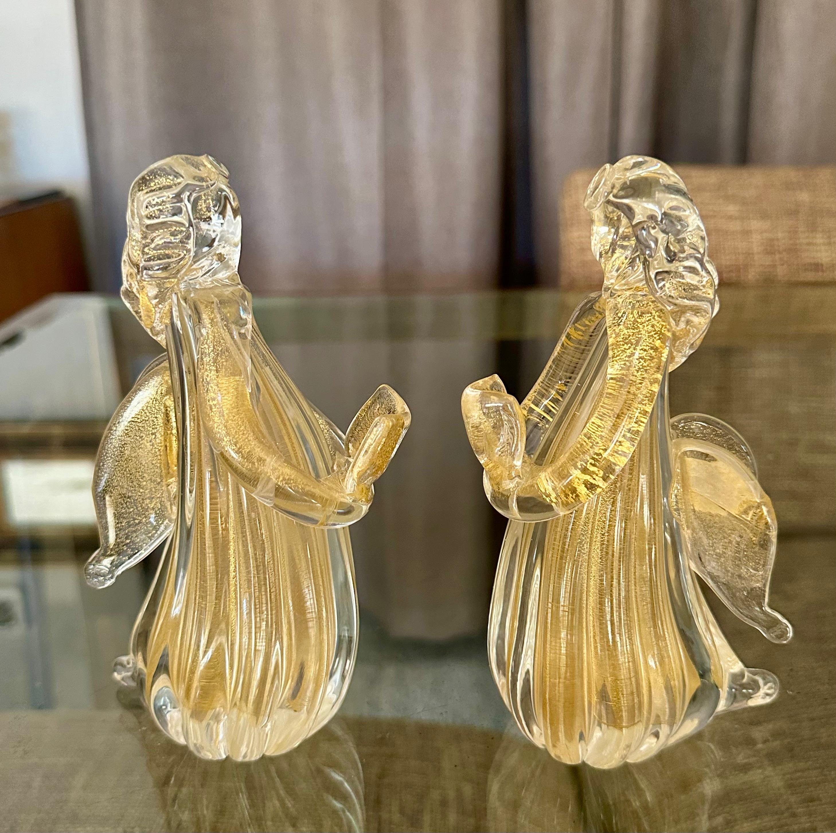 Pair of Murano Italian Venetian art glass Angel figurines singing and holding a choir book . The color of the glass is combination clear with gold inclusions throughout.  As each is hand blown Angels are slightly different sizes. 
