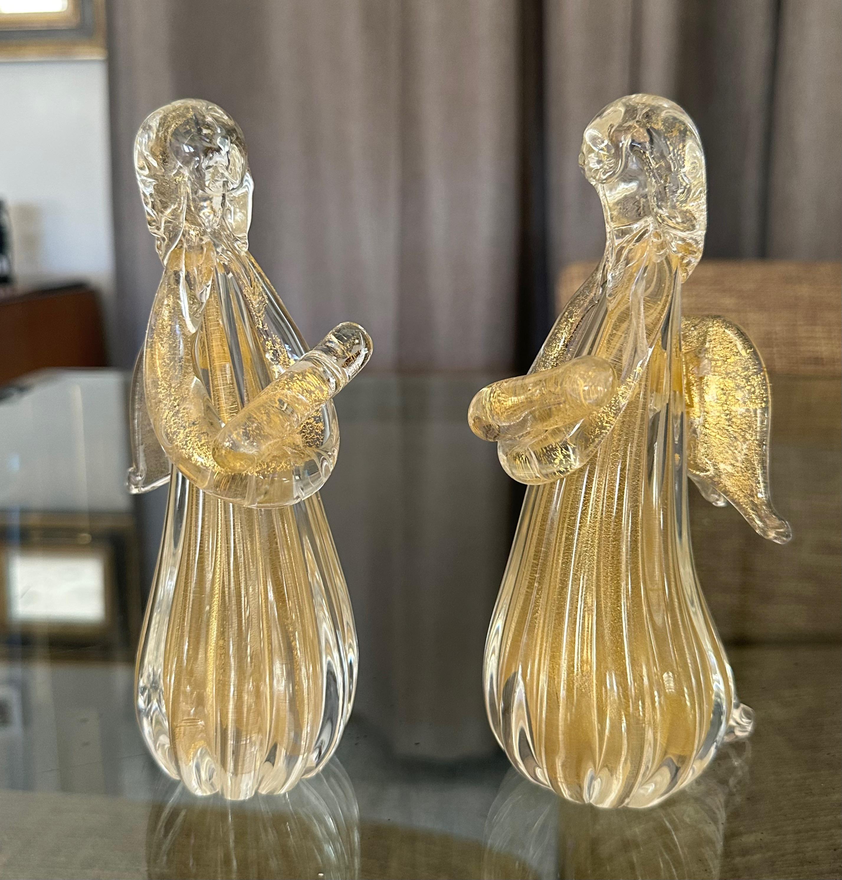 Coppia di statuette di Art Angels in vetro soffiato a mano di Murano, ciascuna con una pergamena in mano. Il colore del vetro è chiaro con inclusioni dorate.  



