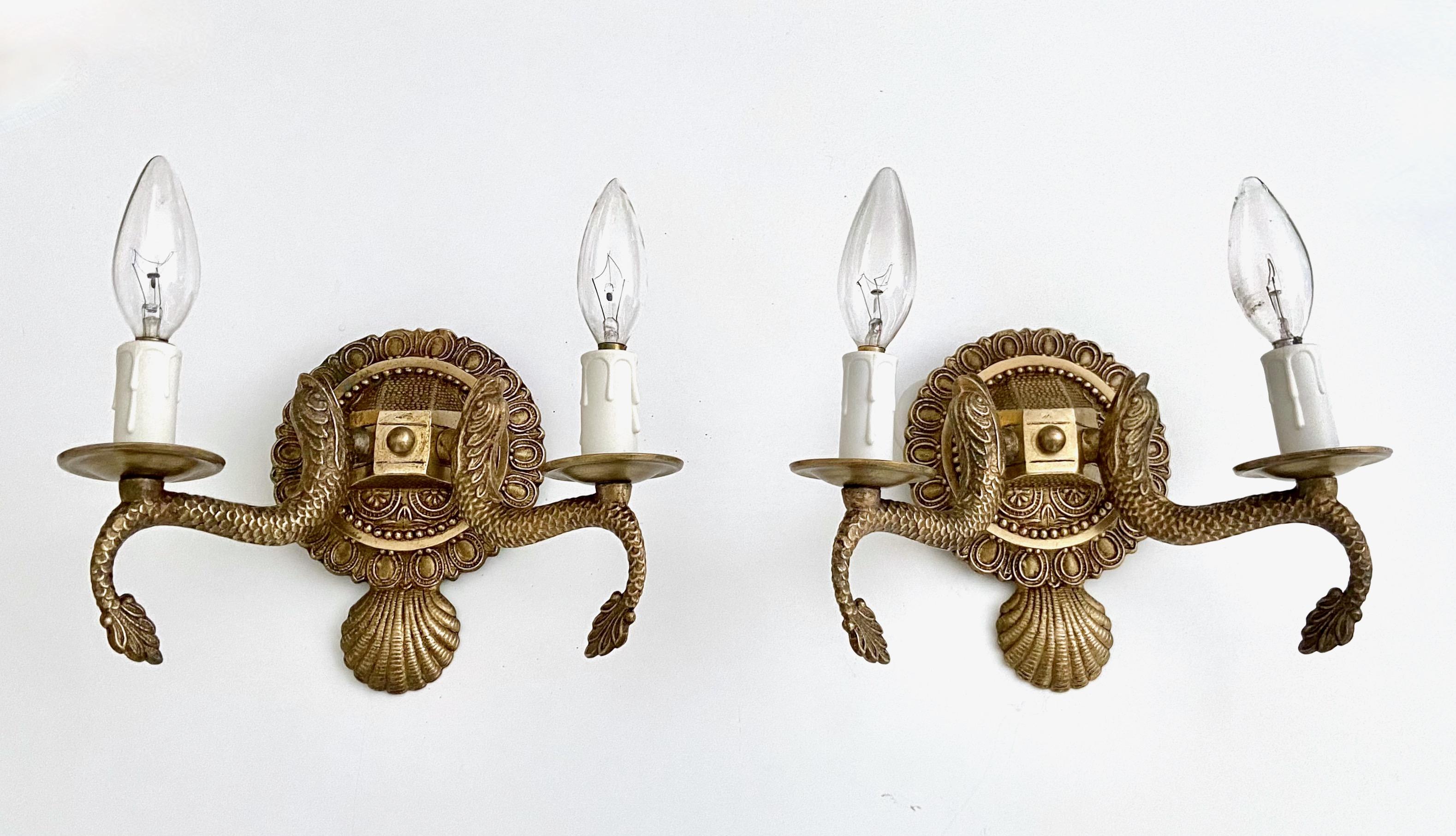 Pair of European two-light neoclassic style brass wall sconces with dolphin and claim shell motif. Expertly crafted with nice quality detailing throughout. Newly wired with new candelabra sockets. Additional pairs available under separate listing.