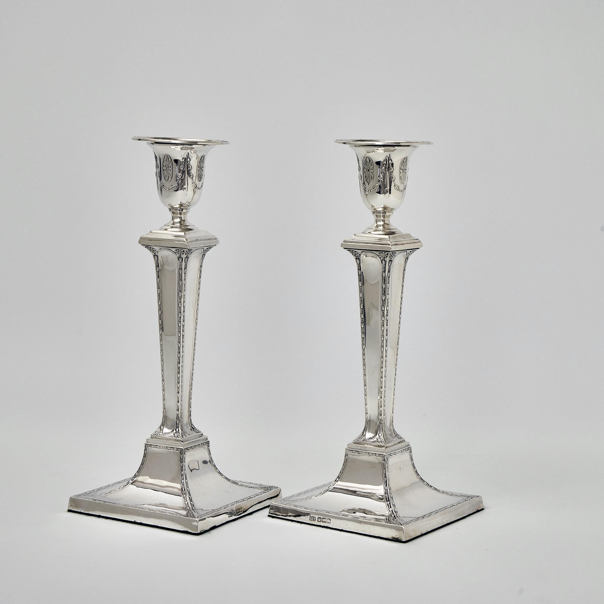 An elegant pair of antique silver candlesticks in the neoclassical style. The panelled columns, bases and candle holders are all decorated with bellflowers, flowerheads and ovoid medallions; all motifs of the neoclassical style.

Neoclassicism was