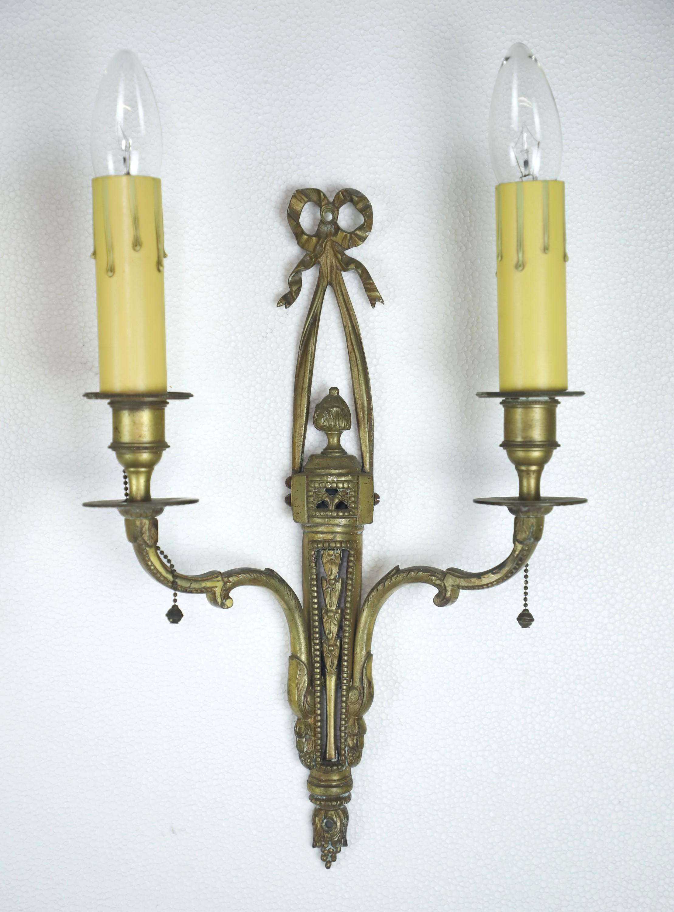 Neoclassical lighting is characterized by elegant, symmetrical designs inspired by ancient Greek and Roman art, often featuring decorative elements such as columns, foliate, and urns. These two arm brass candlestick wall sconces feature ornate