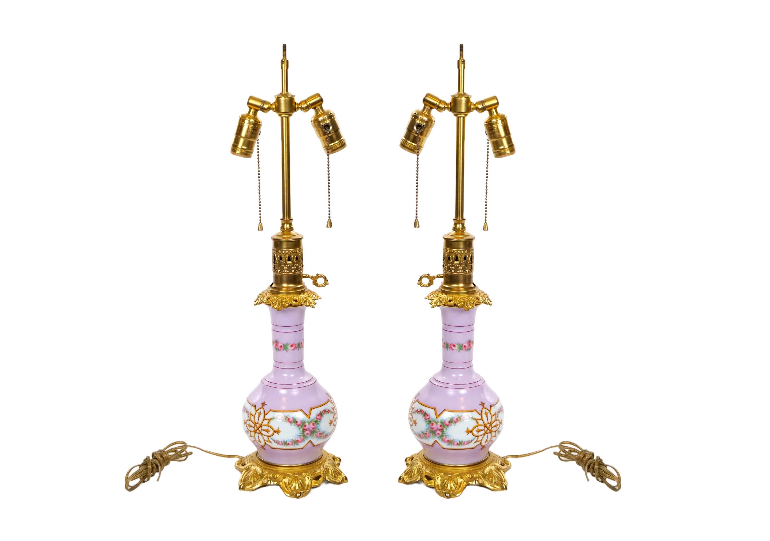 Pair of neoclassical style porcelain with gilt bronze base table lamp. Each lamp features a  baluster shaped, with an ice pink / lavender glazed background resting on a round gilt bronze base with an inner edge of the neck. Each one is in great