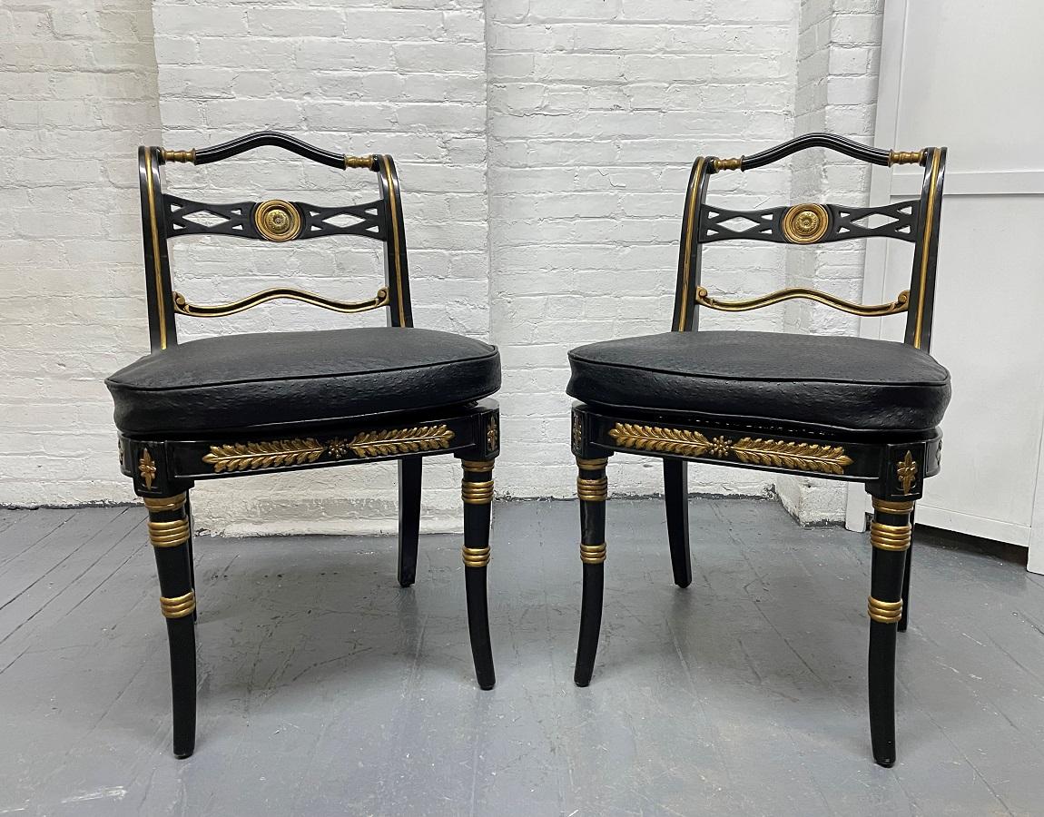 Pair neoclassical style side chairs. The chairs have black lacquered wood frames, a decorative gold pattern with a round bronze insert to the back of the chairs. The chairs also have faux ostrich vinyl covered removable cushioned seats.