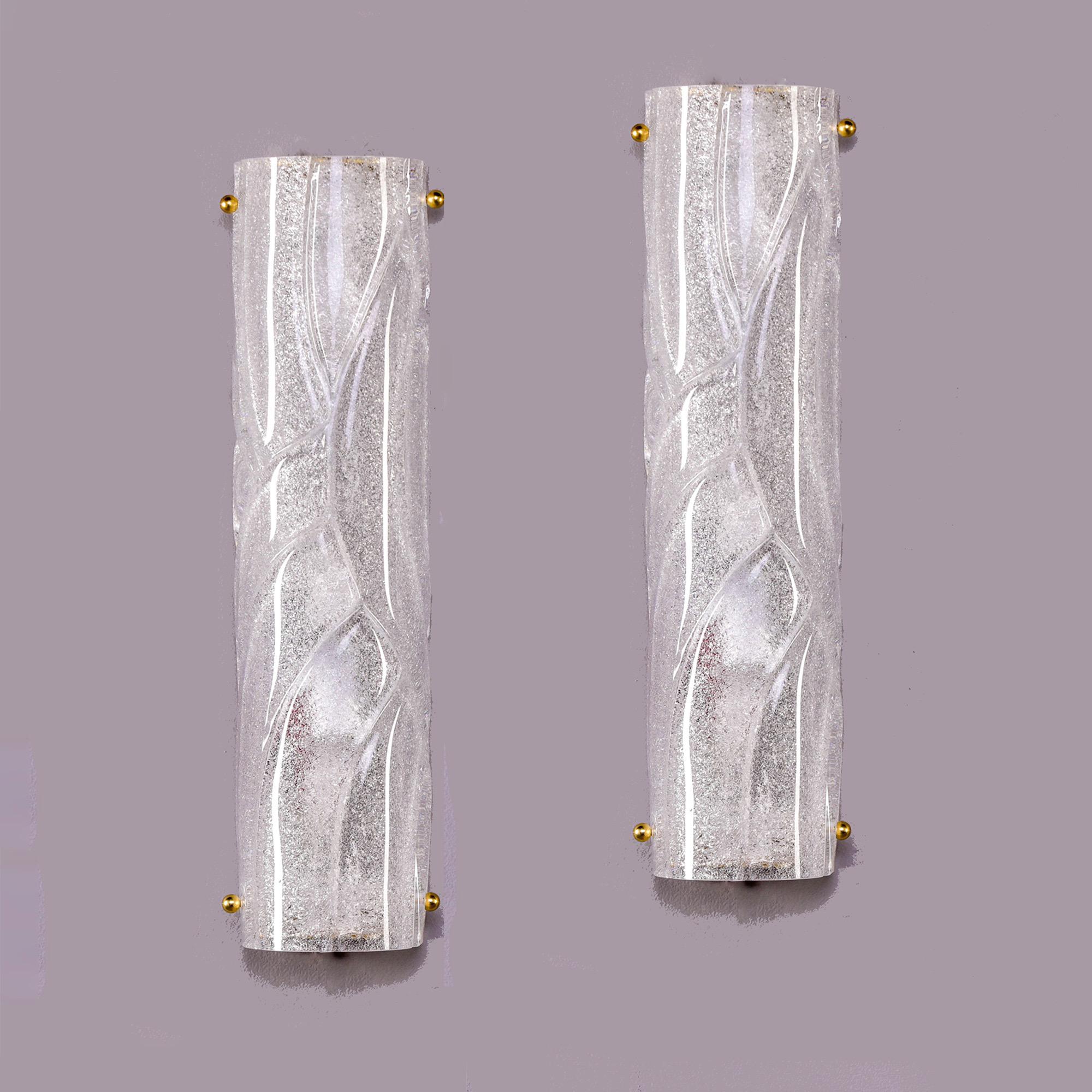 New pair of modern/transitional style Murano sconces in clear, heavy glass with surface swirls and texture. Each sconces has two candelabra sized sockets and brass hardware. Backplates that do not show when sconces are installed are included to