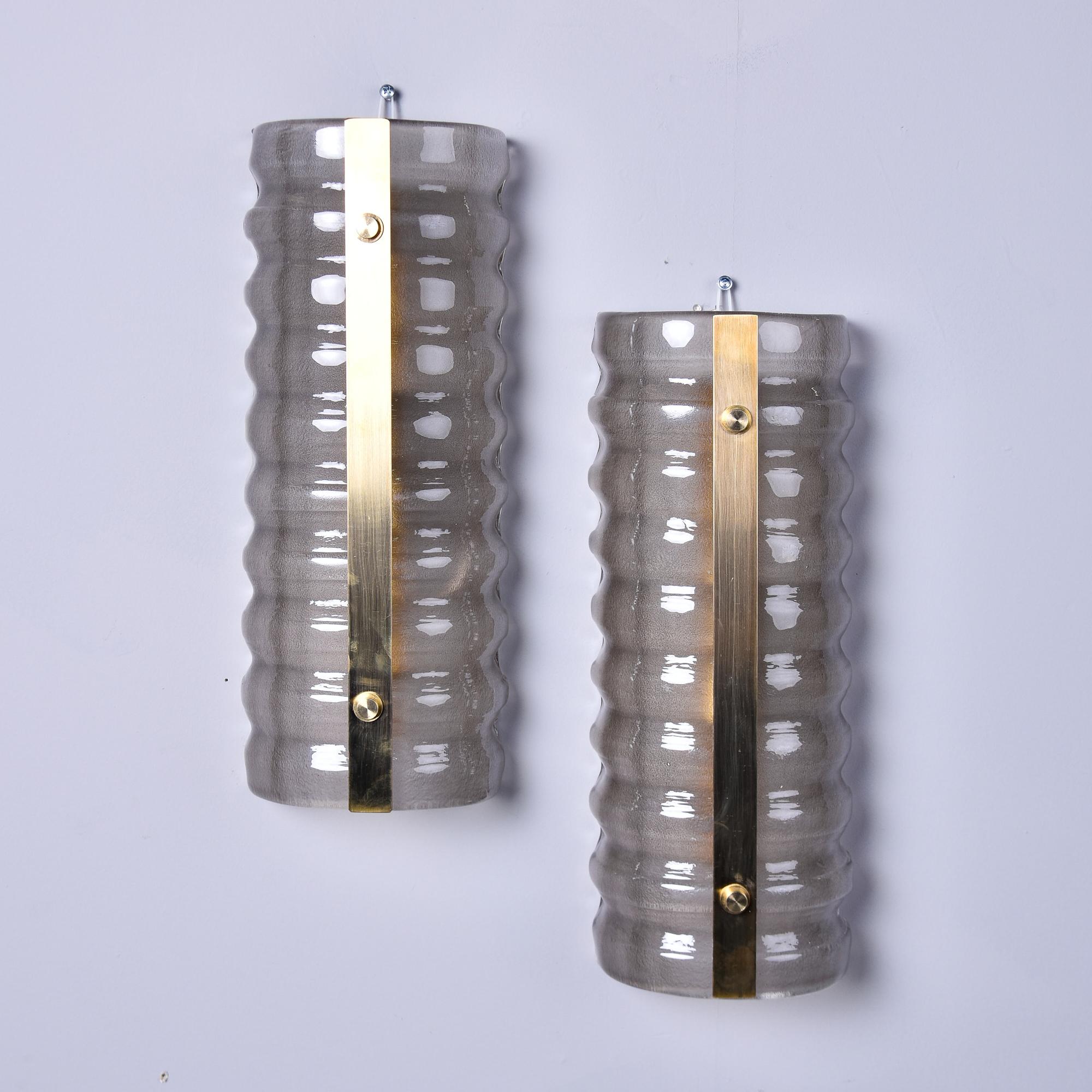 New pair of sconces made in Italy feature handmade Murano glass shades in a smokey taupe color. Each shade thickly ribbed surface and is accented with a vertical brass band.  Sconces each have two standard sized sockets and the electrical wiring has