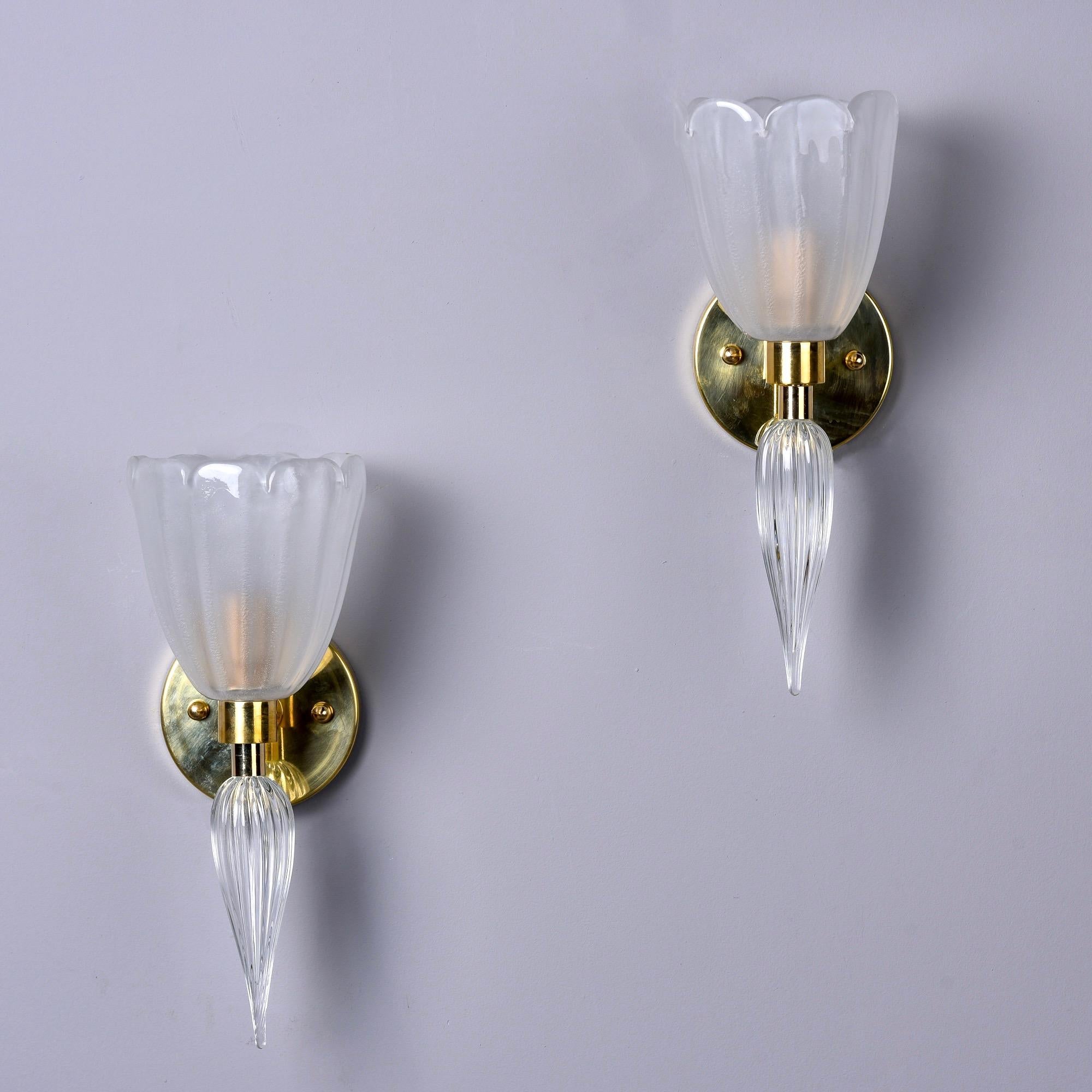 New pair of sconces in Murano glass and brass. Polished brass round backplates and hardware. The sconces feature shades in a semi-opaque white glass with fluted edges and long, clear glass finials. Wired for US electrical standards. Sold and priced