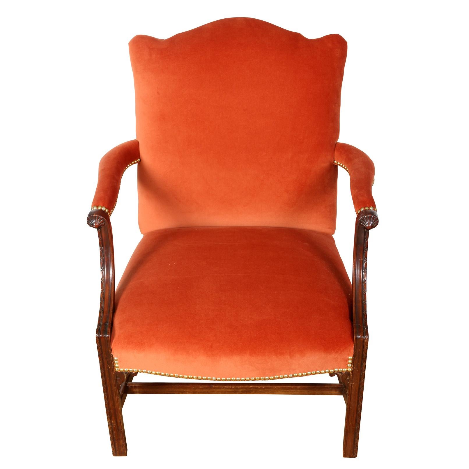 A pair of vintage George III style armchairs, newly upholstered in orange velvet.  A sunny update to a traditional pair of library chairs with a shaped back, upholstered arm rests ending with carved detail, and straight wood legs with straight