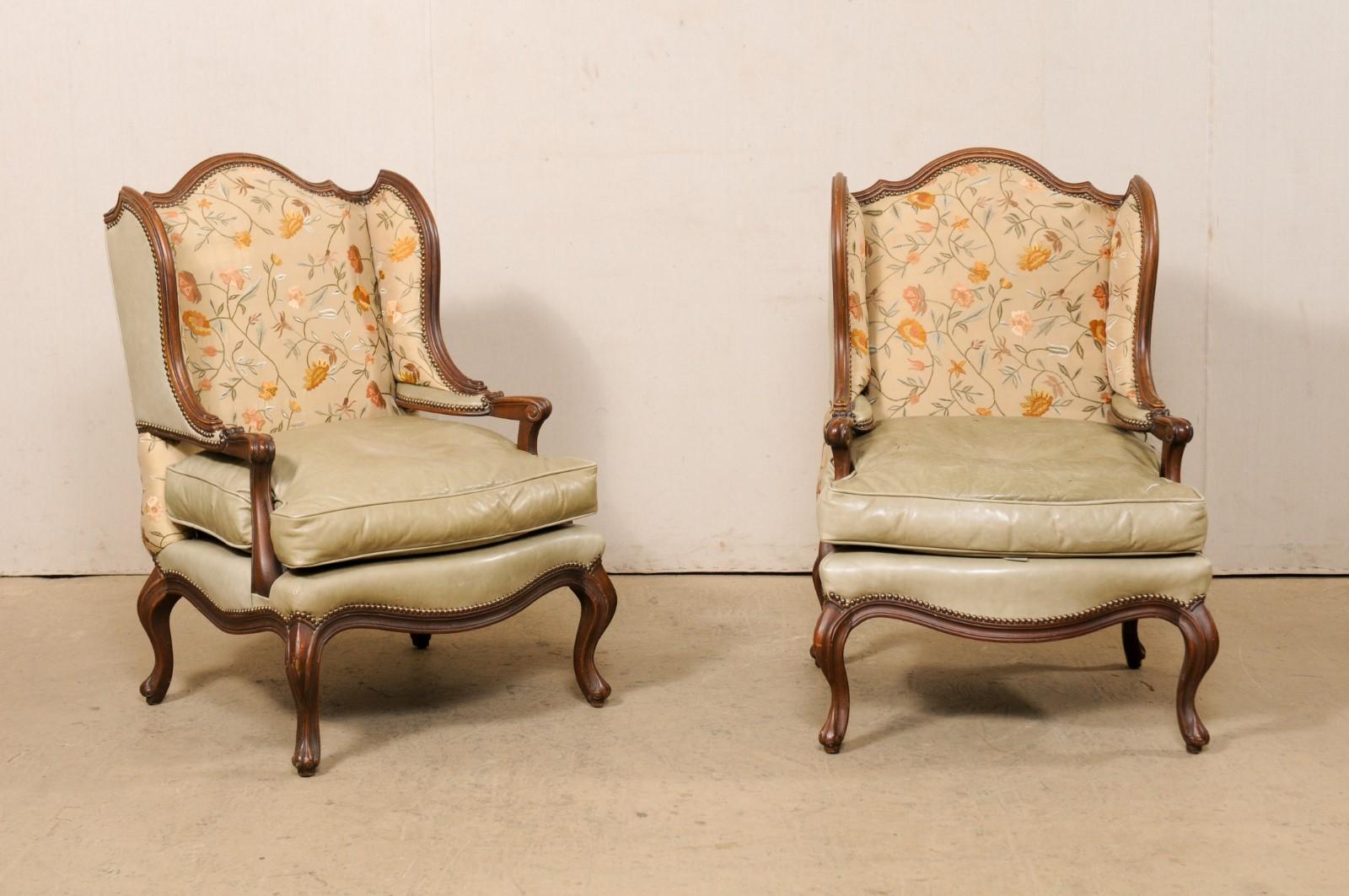 A pair of French style winged-back carved-wood and upholstered armchairs from the mid 20th century. This vintage pair of bergère chairs from America have been created in the beautiful styling inspired by the French with each featuring winged-backs