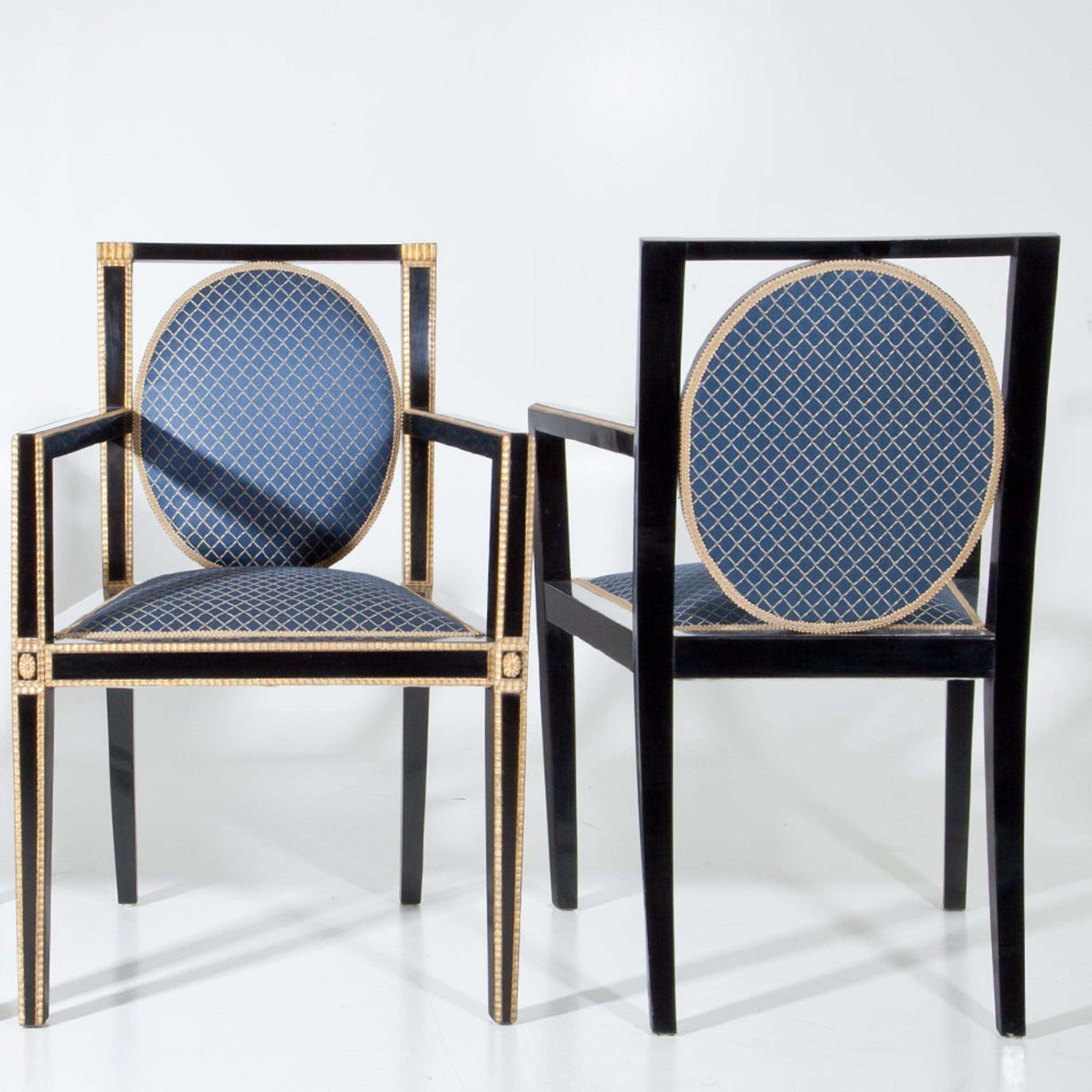 Pair o ebonized armchairs of the Viennese Secession with gilt wavy moldings around the legs, armrests and backrests. These show an upholstered medallion-shaped back framed by black stiles and rails. The blue upholstery with gold rhomboid pattern is