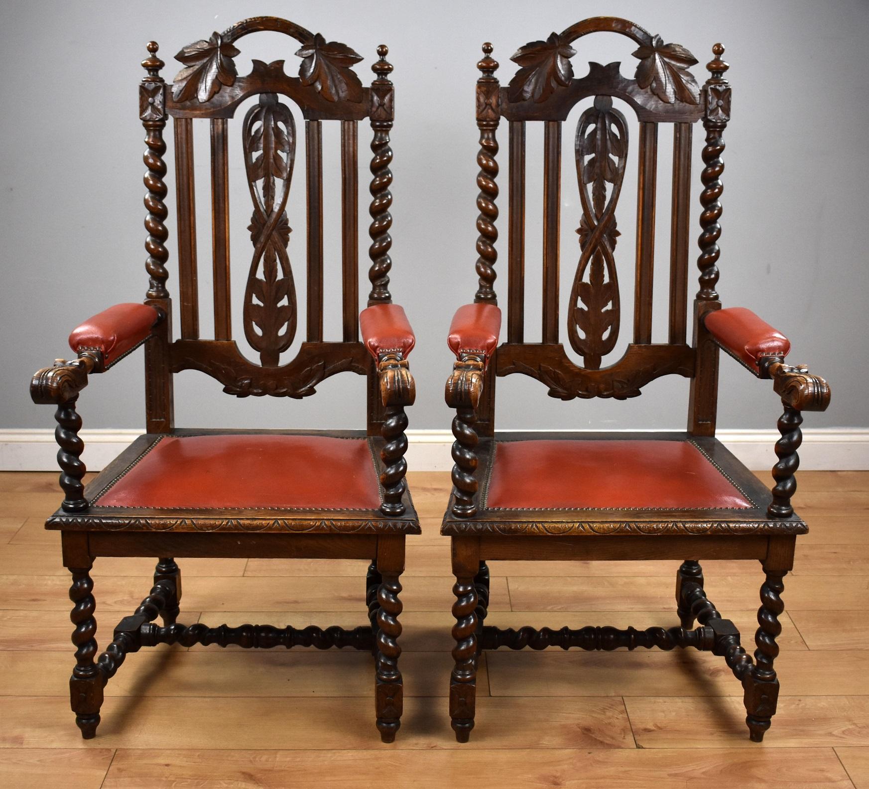 Pair oak barley twist arm chairs in good condition. The chairs have carved leaves to the top and centre of the backs, each side has barley twist columns with red upholstered arms with close studding to the edge and over stuffed seats. The chairs