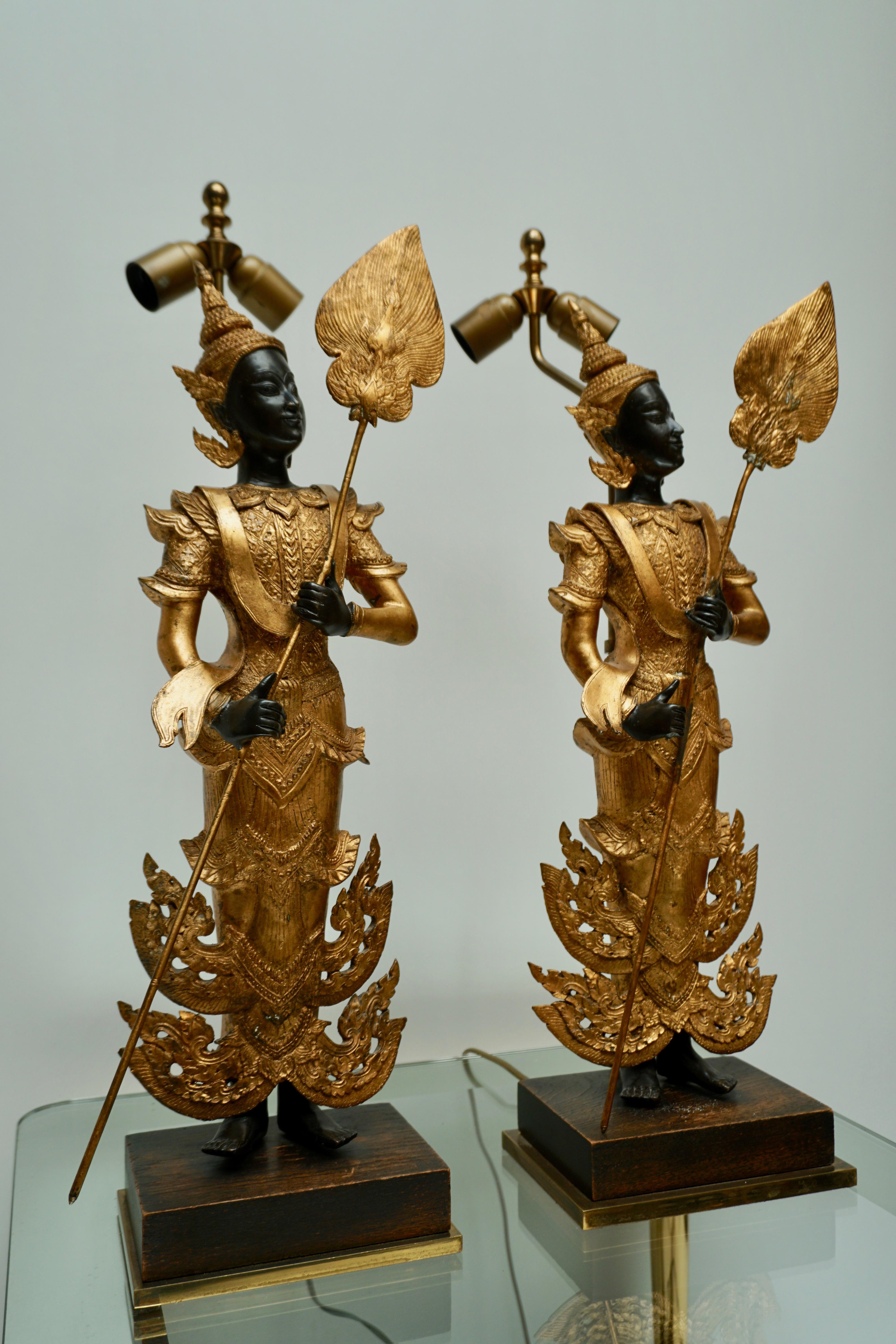Ein großes, beeindruckendes Paar wunderschön lackierter und vergoldeter Bronzefiguren. Museum auf Holz- und Messingsockel montiert und Mitte des 20. Jahrhunderts in Lampen umgewandelt. Neu verkabelt. Thailand, 20. Jahrhundert. 
Das Maß für die