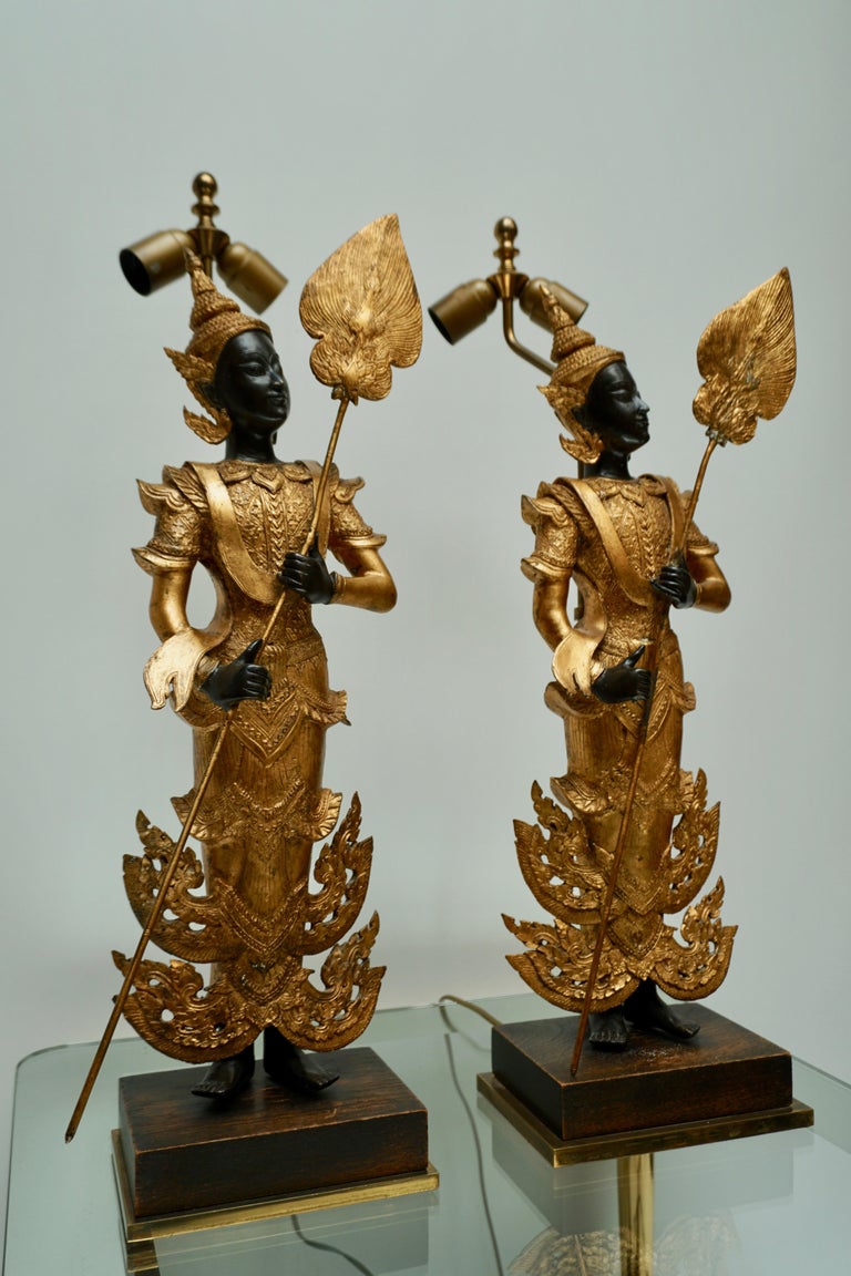 A large impressive pair of beautifully lacquered and gilded bronze figures. Museum mounted on wood and brass bases and converted to lamps in the mid-20th century. Newly re-wired. Thailand, 20th century. 
Measurement for just the figure is 64 cm
