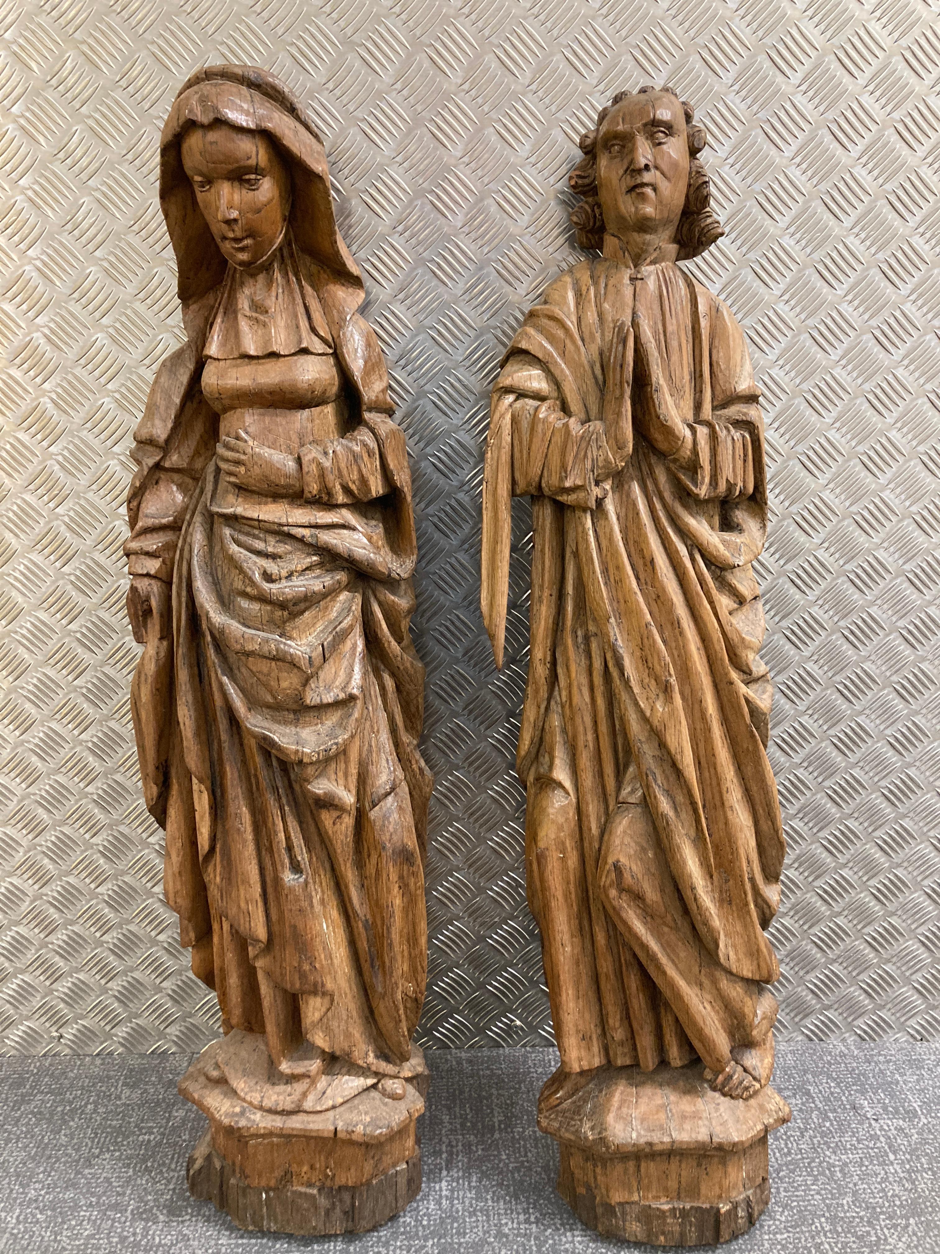 A Pair of Late 15th or Early 16th Century Oak Saints carved in high relief and raised on polygonal bases. The female depicted standing in contrapose with lowered head wearing a draped mantle and neckerchief over a long gathered robe. The male with