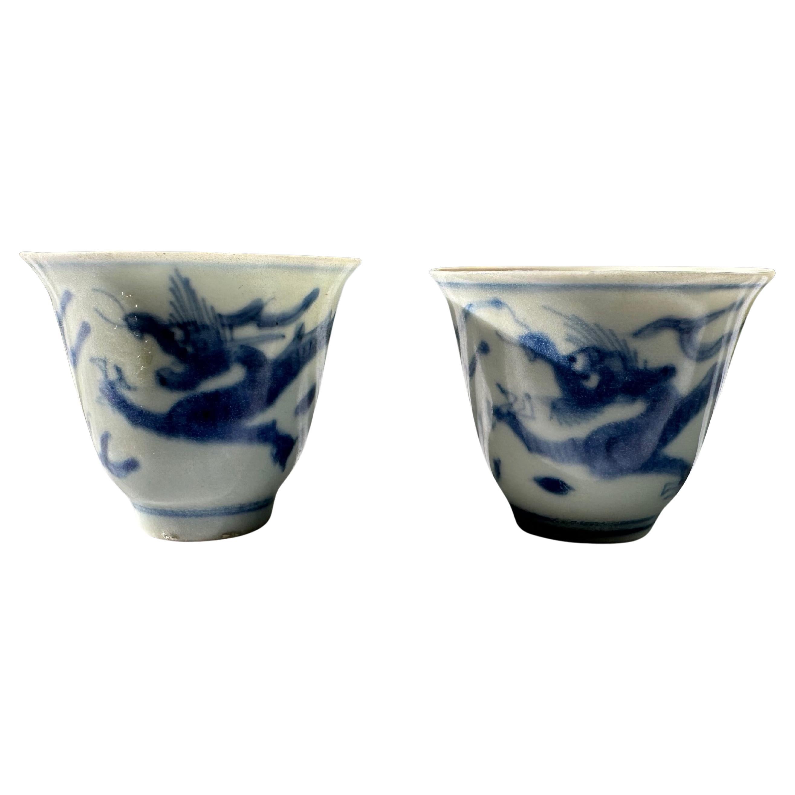 Pair of 17th Century blue and white wine cups from the Hatcher Collection painted with a dragon leaping through cloud scrolls to grasp a flaming pearl. The cups are delicately potted with fluted rims, with a double line border around the foot and a