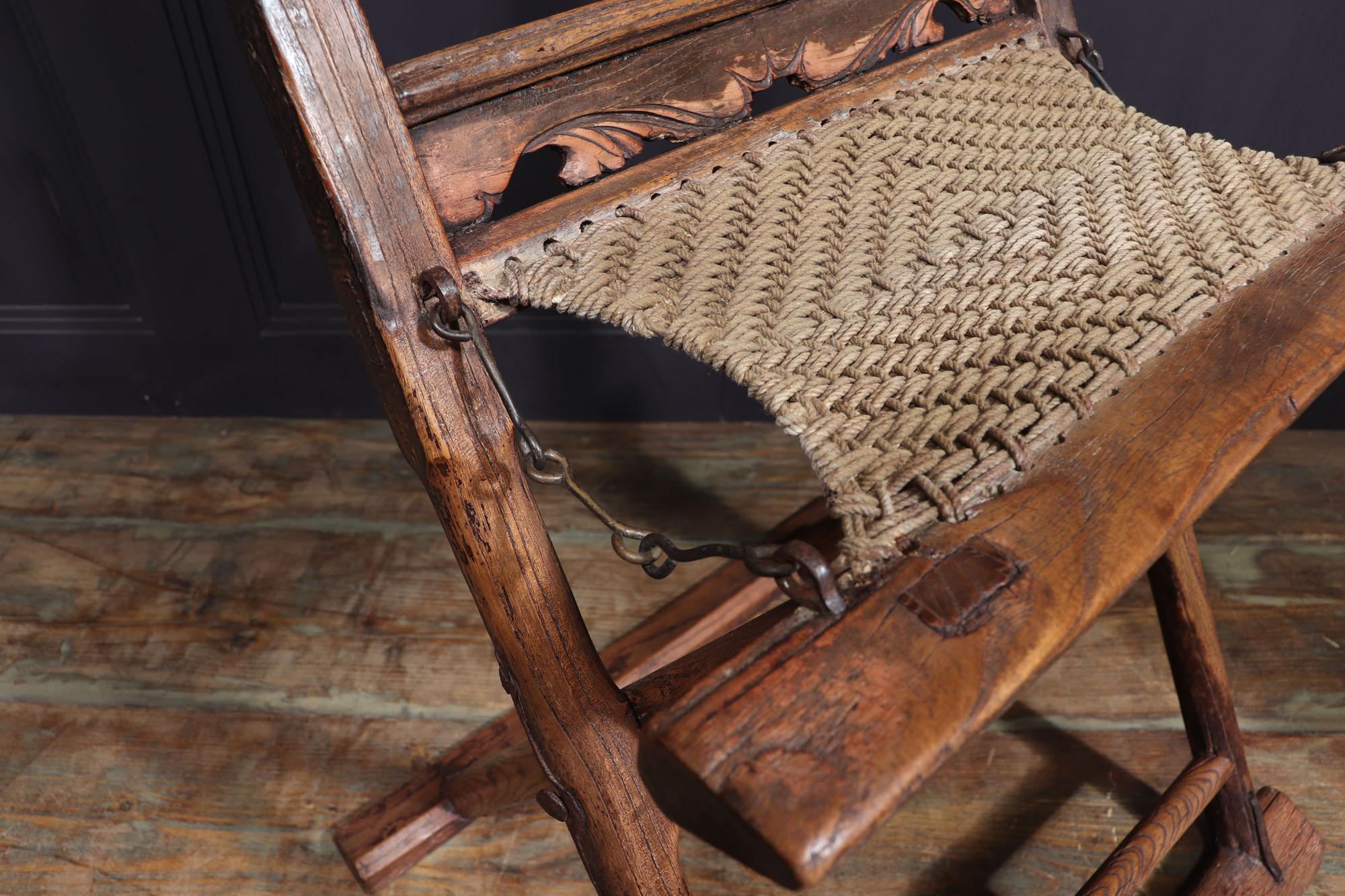 A pair of folding chairs produced in the early 17th century from elm a hardwood that is native to China, narrow rail supports and curved uprights, hinged rounded legs with rectangular base stretchers, woven and strung seat, parts of original lacquer