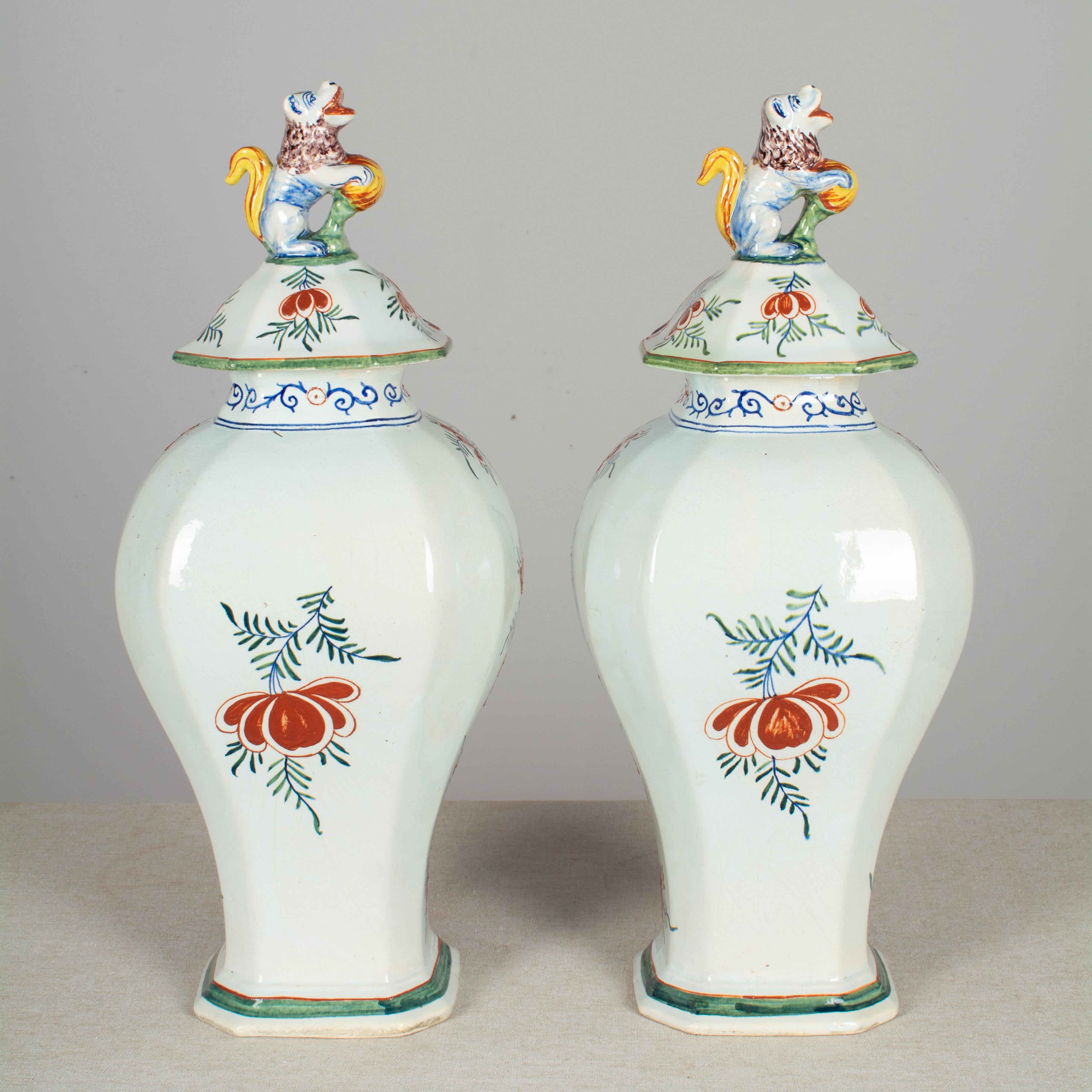 A pair of 17th century Delft faience polychrome painted tin glazed ginger jars with octagonal urn form and lids topped with sculptural foo lions. Bold design with elaborate, colorful hand painted decoration in thick raised relief. The front panels