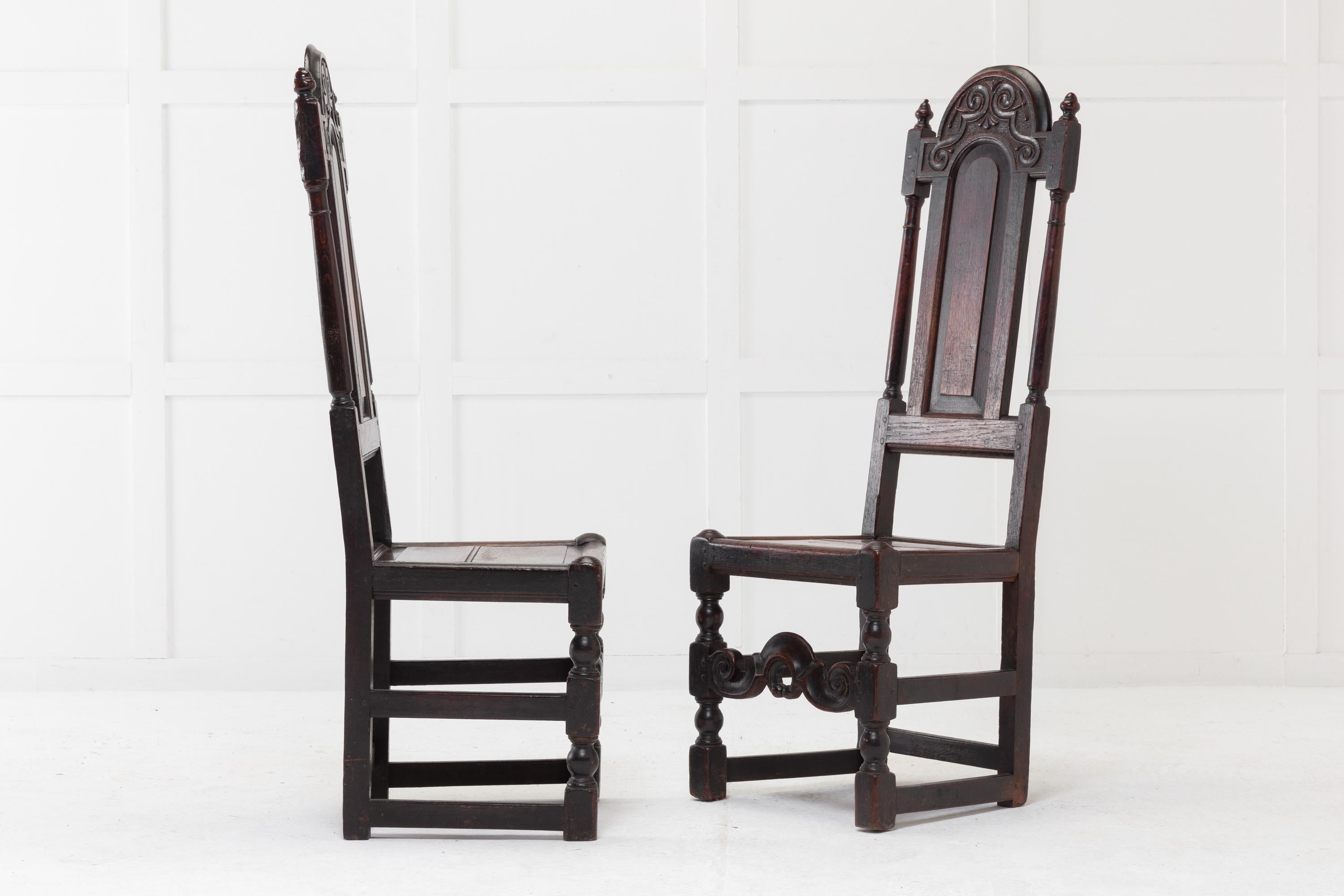 A rare pair of 17th century English oak side chairs having high backs, beautifully carved top rails and wide panelled back splats flanked by turned supports with finials. Original solid wooden seats made of two moulded panels. Traditional stretchers