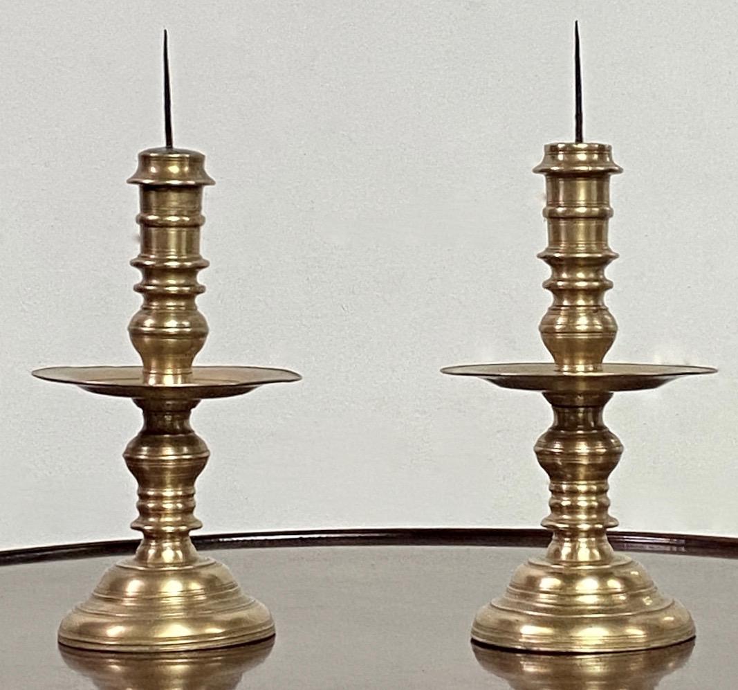 Coppia di candelabri in bronzo tornito della fine del XVII secolo (olandesi o tedeschi) con piastre di gocciolamento e prese in piombo con pinnacoli in ferro.  
Nel complesso ottime condizioni originali.   13,5