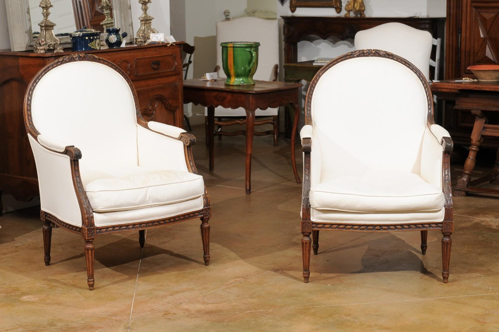 A pair of French Restauration period walnut bergères chairs from the mid 19th century, with carved foliage and twisted ribbons. Created in France during the second quarter of the 19th century, each of this pair of bergères features an arching back