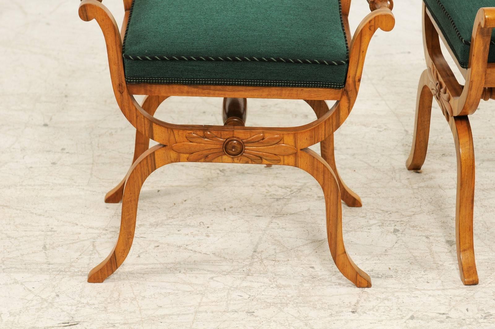 A pair of mid-19th century Austrian Biedermeier stools with green upholstered seats and X-form base. Each of this pair of Biedermeier stools features a new green upholstered rectangular seat, safely secured by two delicately out-scrolled arms with