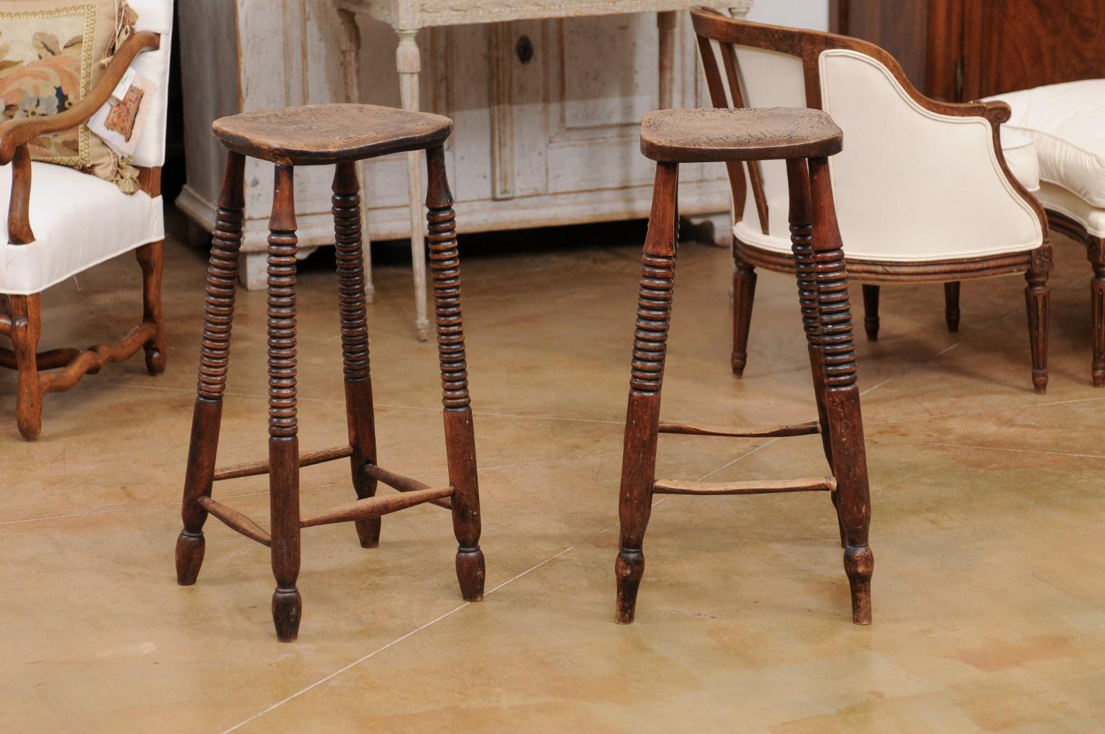 A pair of rustic French wooden bar stools from the late 19th century, with spool legs and weathered patina. Created in France during the third quarter of the 19th century, each of this pair of bar stools features a nicely aged square top sitting